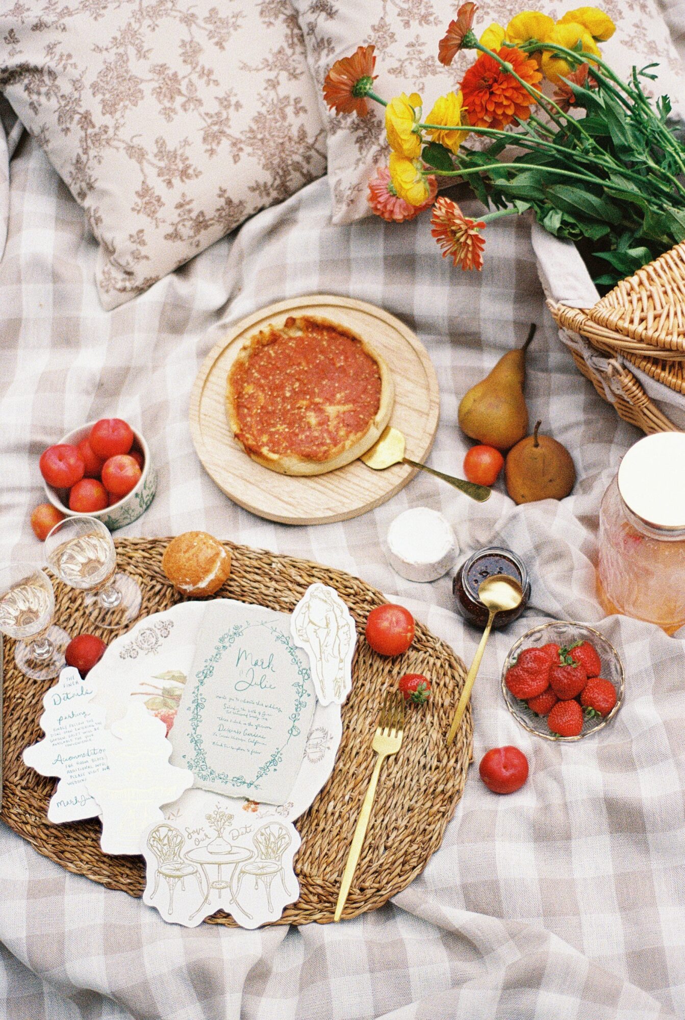 A picnic setup with a plate of pancakes, strawberries, and a bouquet of flowers on a checkered blanket.