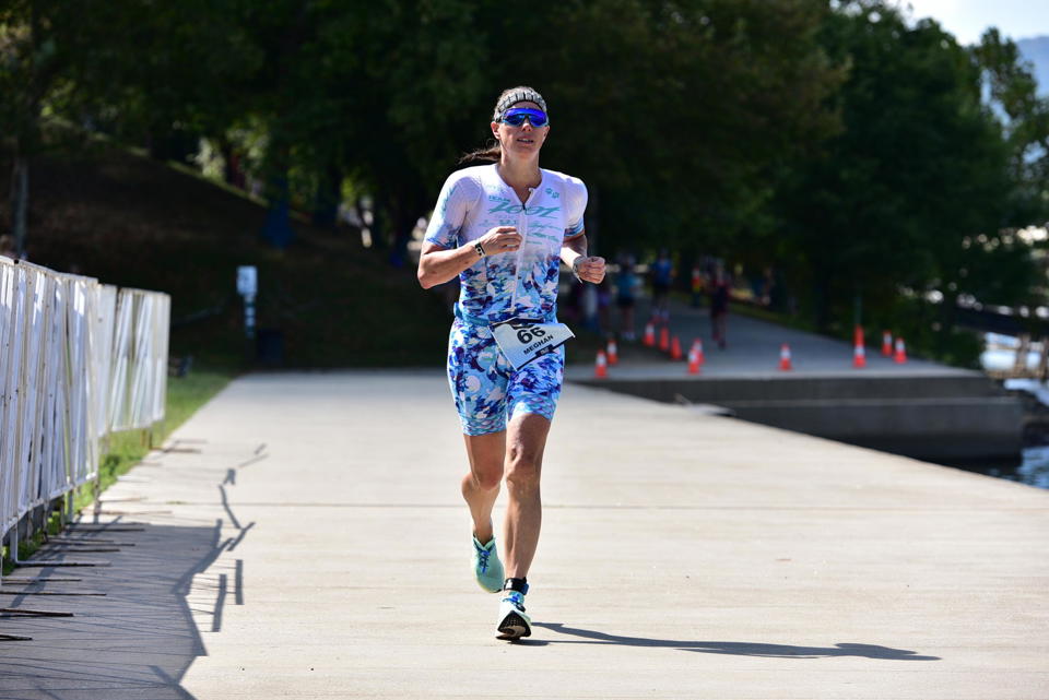 Person running on a paved path wearing a white shirt, blue patterned shorts, and sunglasses, with trees in the background.