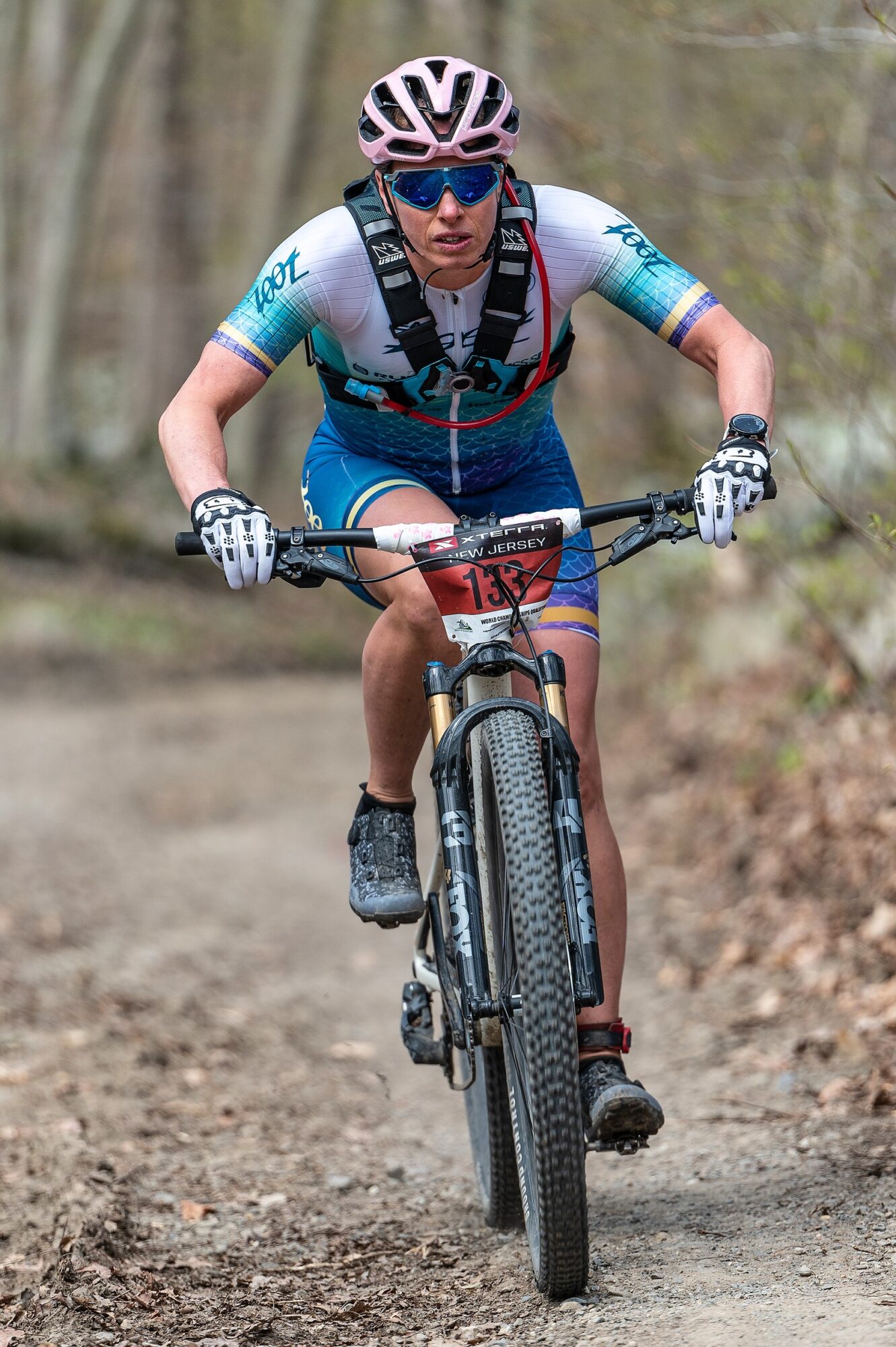 Cyclist wearing helmet and sunglasses riding mountain bike on dirt trail in forest