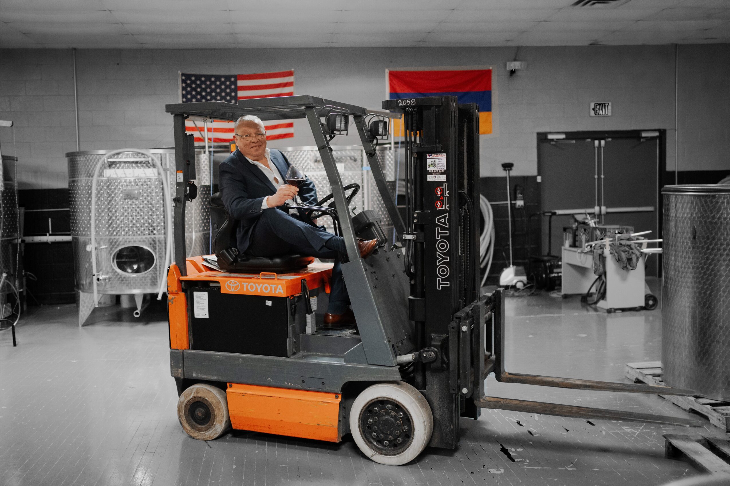 Person operating a forklift indoors with American and Russian flags in the background.
