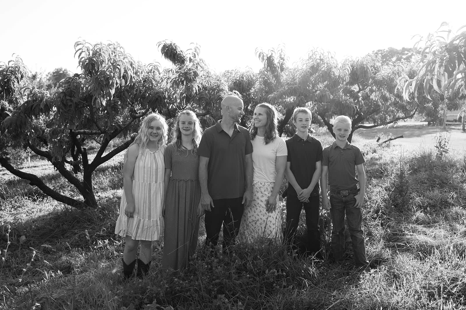Group of seven people standing outdoors in a grassy area with trees in the background.