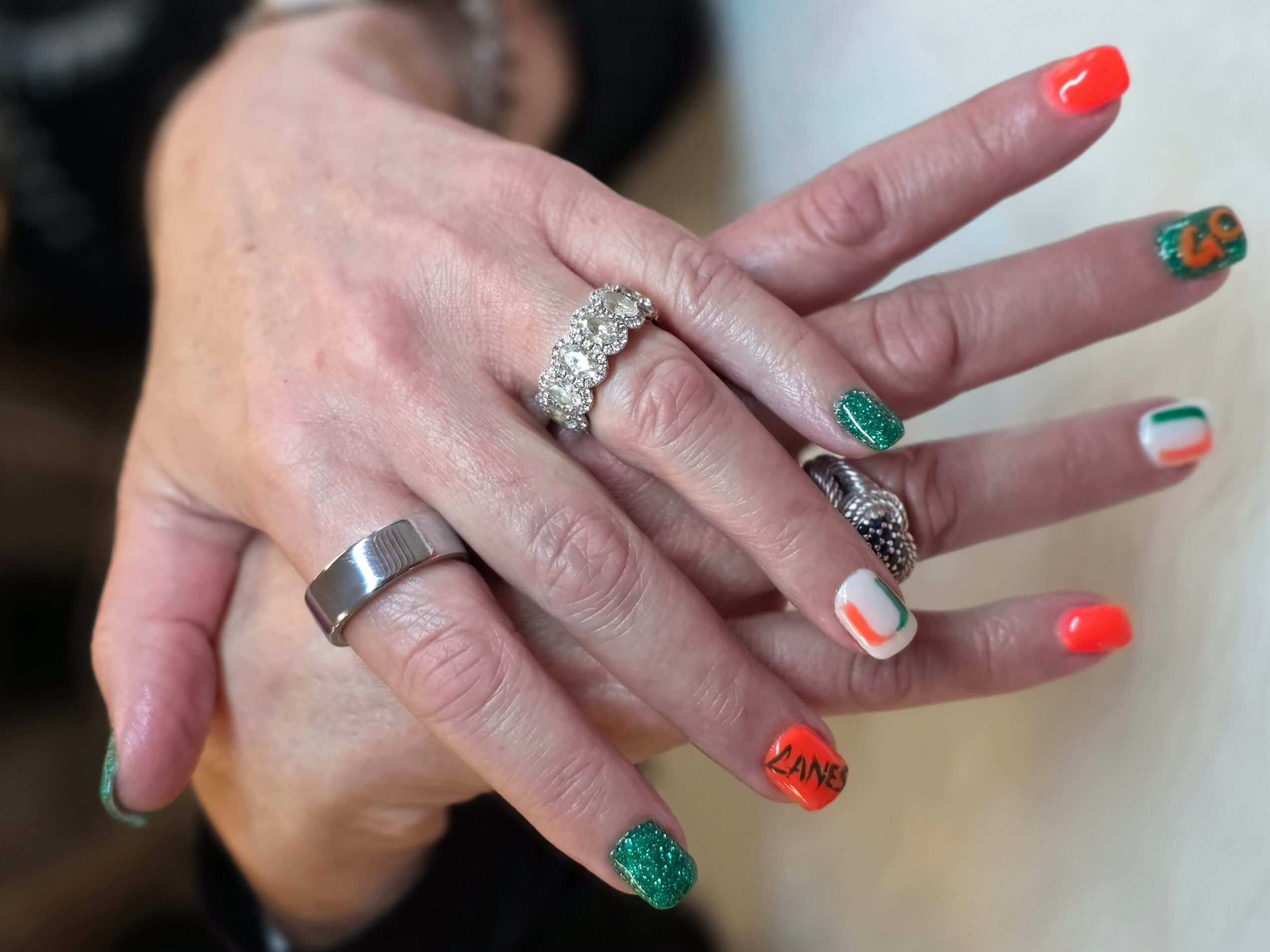 Close-up of hands with rings and colorful nail polish, including red, green, and striped designs.