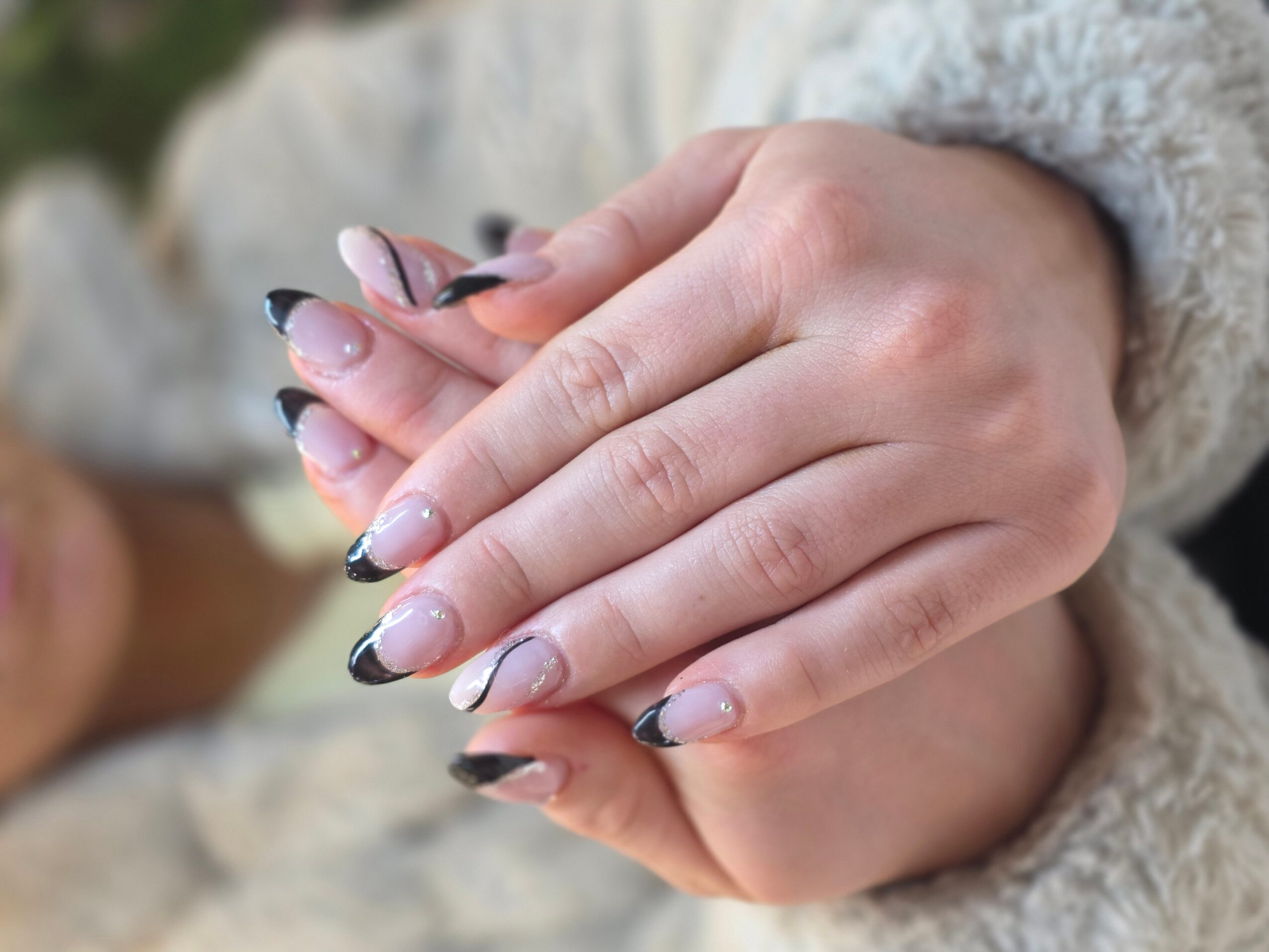 Close-up of hands with manicured nails, one hand resting on the other, wearing a cozy sweater.