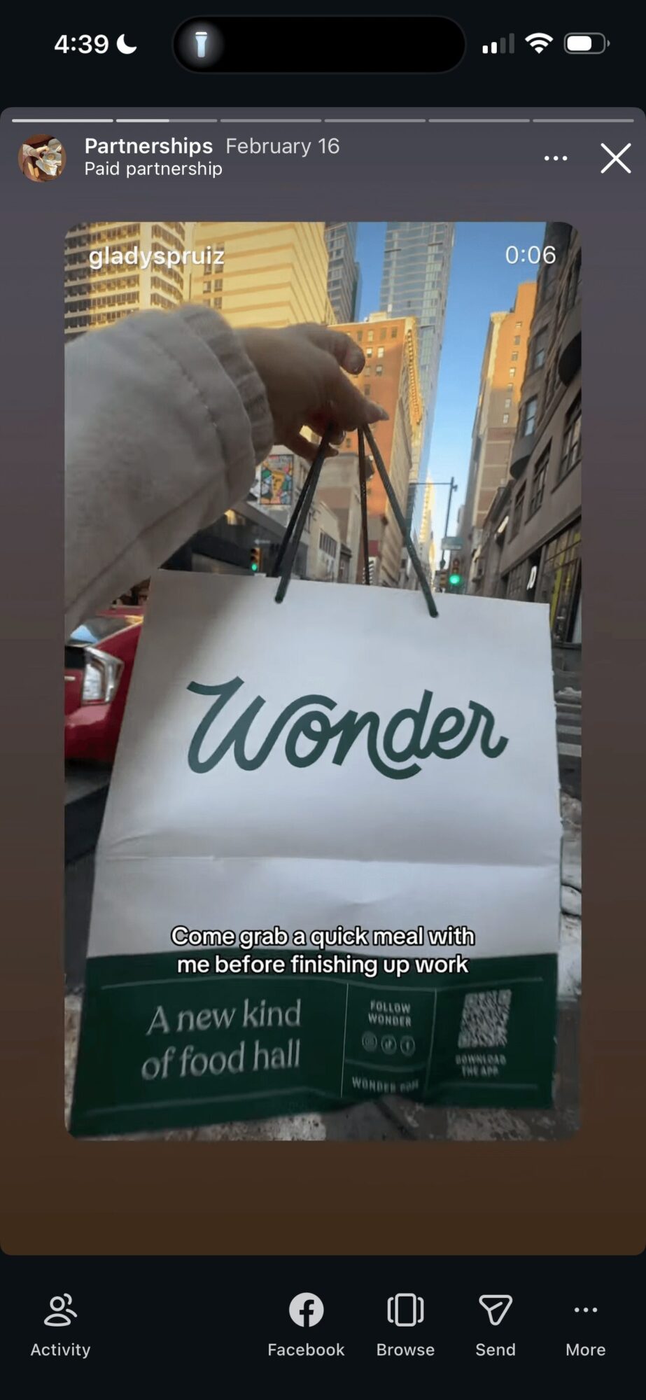 Person holding a white shopping bag with 'Wonder' written on it, city buildings in background.
