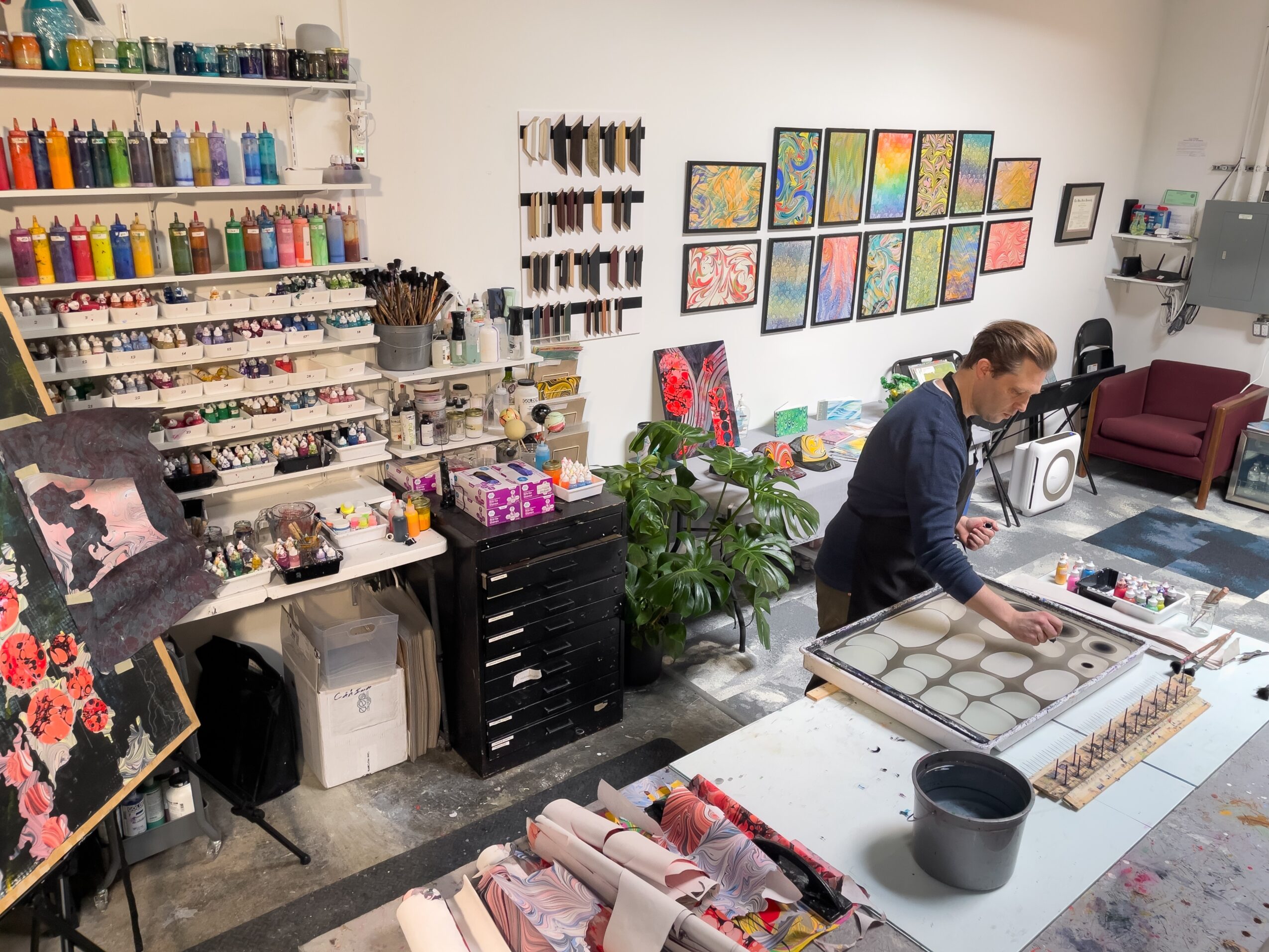 Art supplies and paintings displayed in an art studio with a person working at a table.