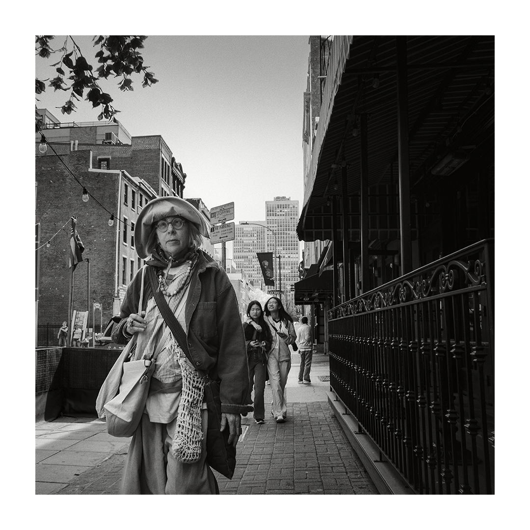 Woman walking on city sidewalk with buildings and other pedestrians in background.