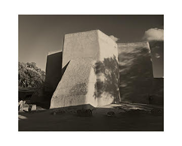 Large concrete building with geometric shapes, shadows, and clouds in the sky, in black and white.