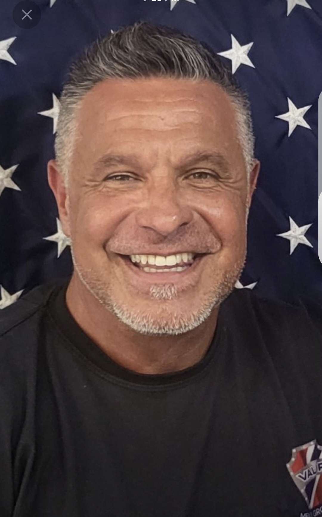 Smiling man with short gray hair and beard, background of stars, wearing a black shirt.