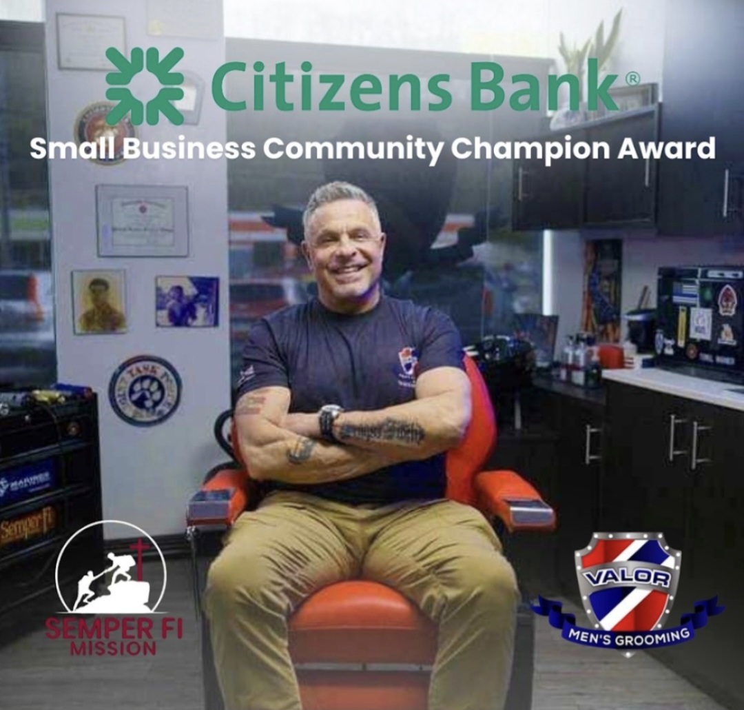 Man sitting in barber chair smiling, with Citizens Bank logo and awards behind him, in a barbershop. Alt text word count: 20