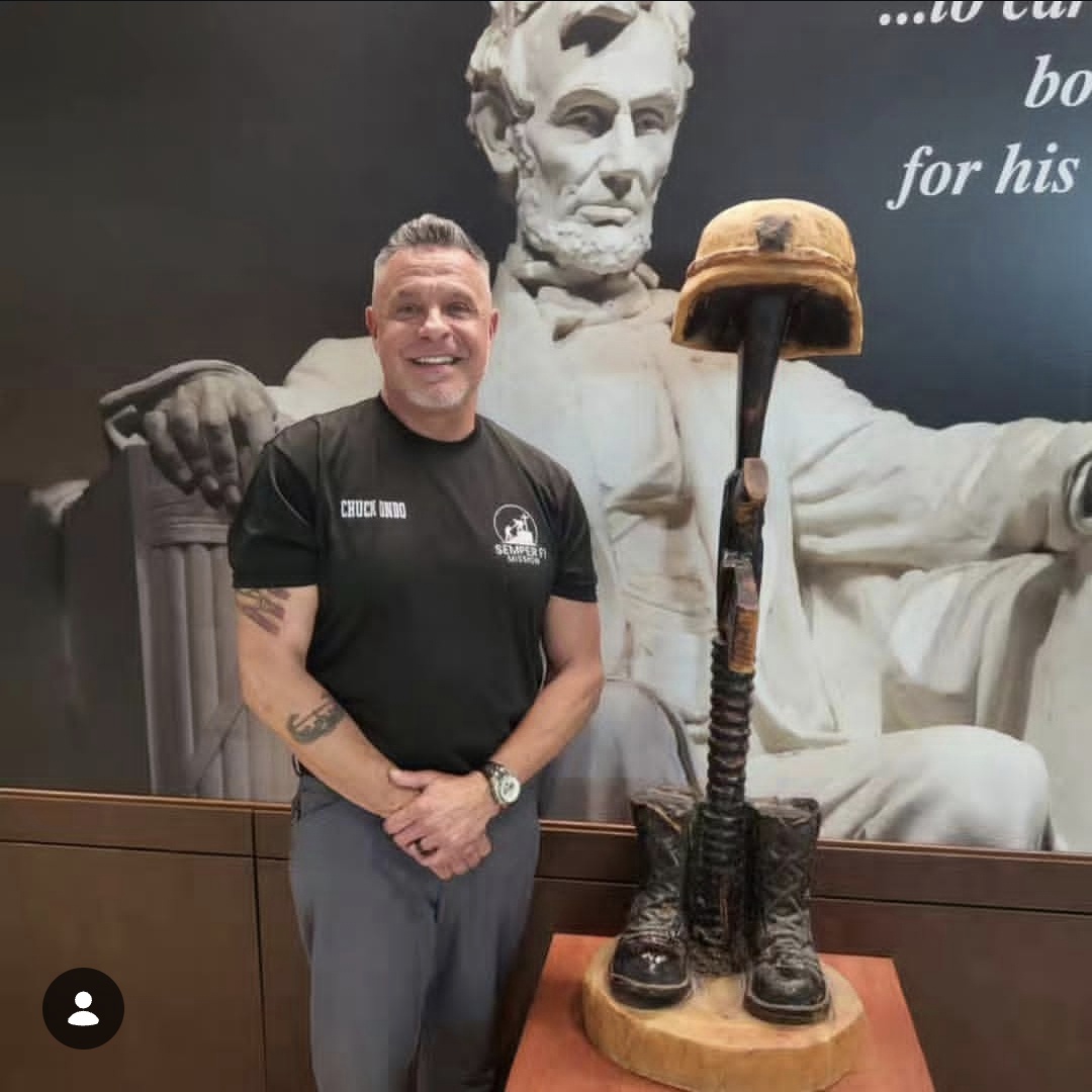 Man standing in front of a large statue of Abraham Lincoln with a helmet and boots, smiling, in a museum setting.