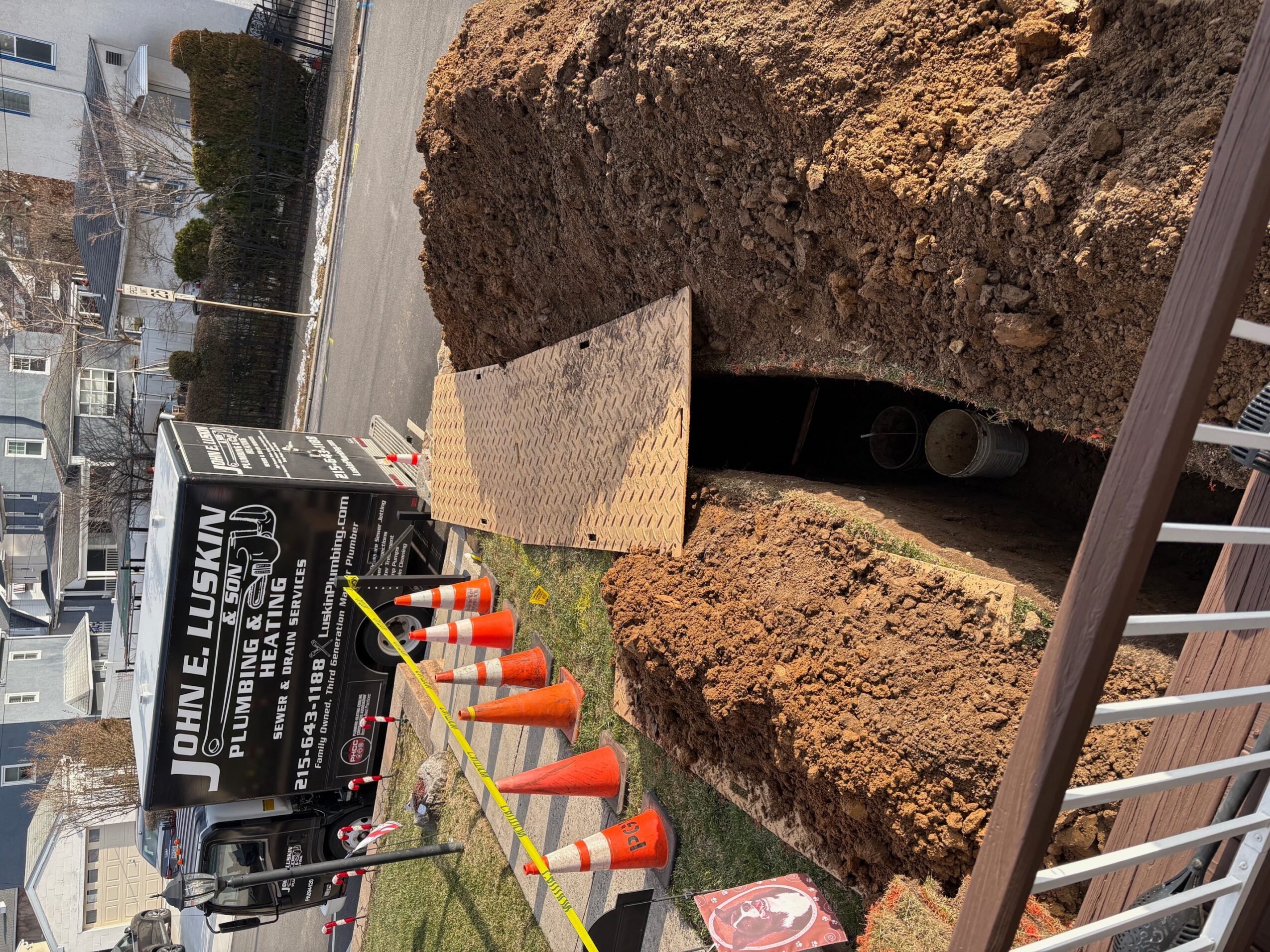 Construction site with large dirt pile and orange traffic cones, partially blocking a sidewalk and street.