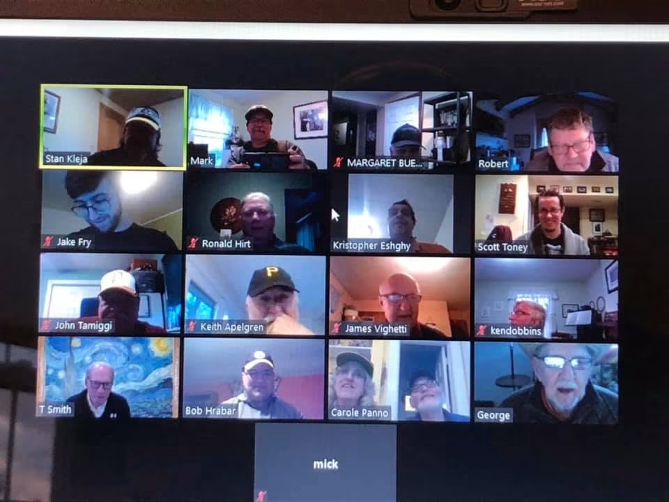 Zoom video call with 20 participants, some wearing headphones, in various indoor settings, with names displayed below each person.