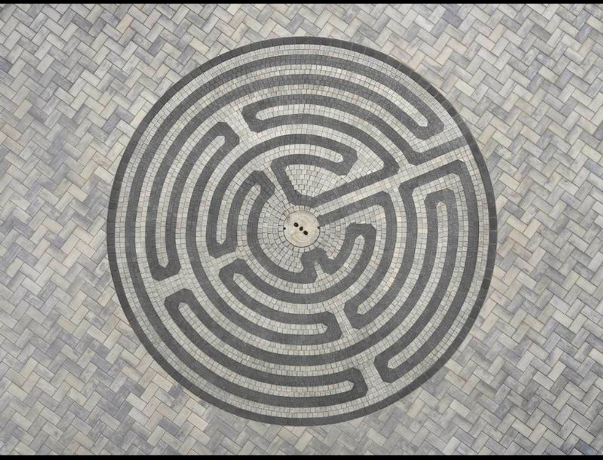 Circular maze pattern on ground with brick paving background