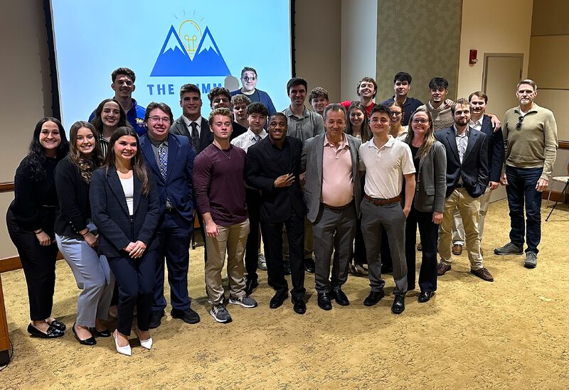 Group of people standing together in a room with a presentation screen behind them, smiling for a photo.