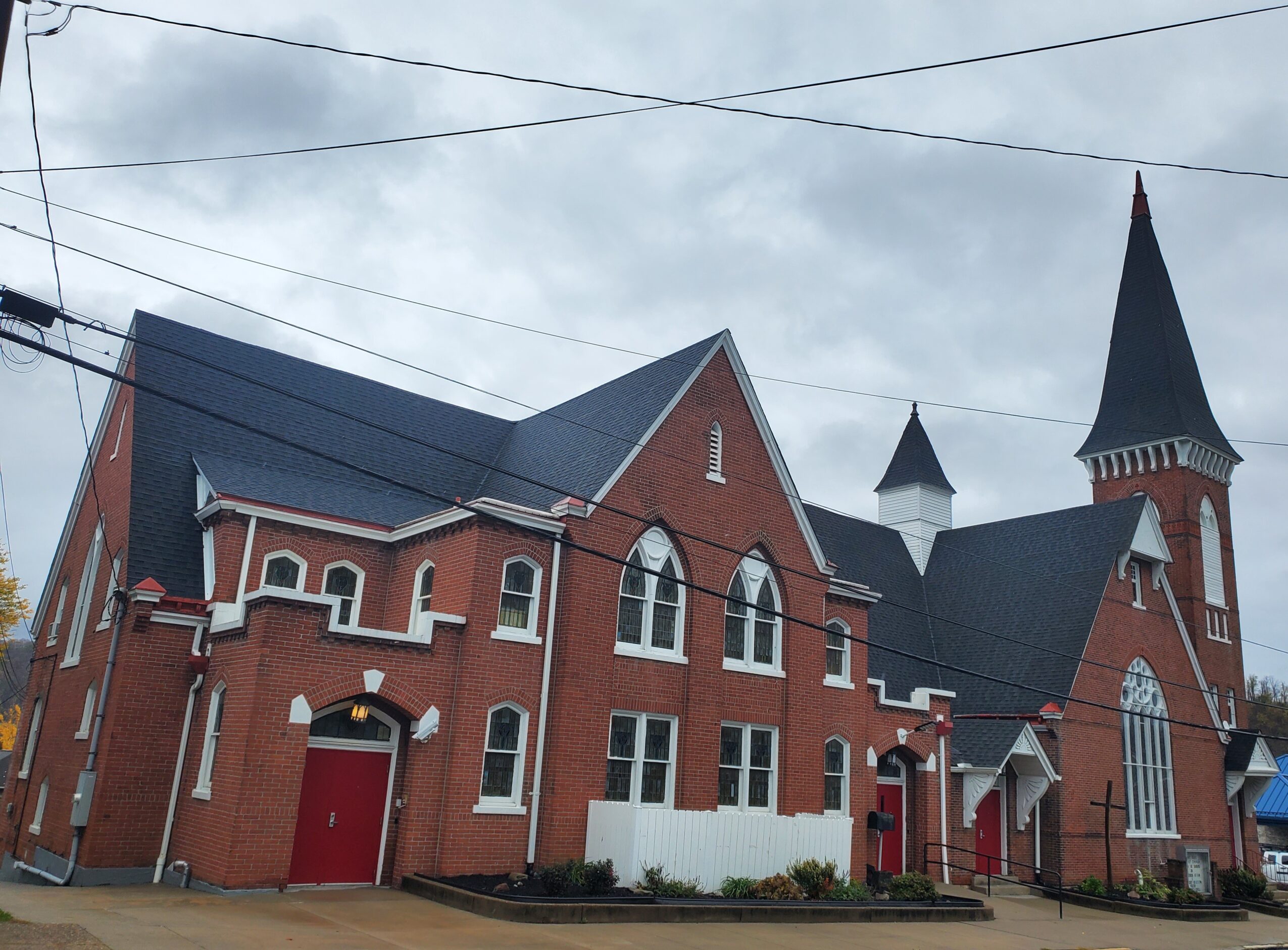 Brick church with tall steeple, pointed roof, and arched windows under cloudy sky.