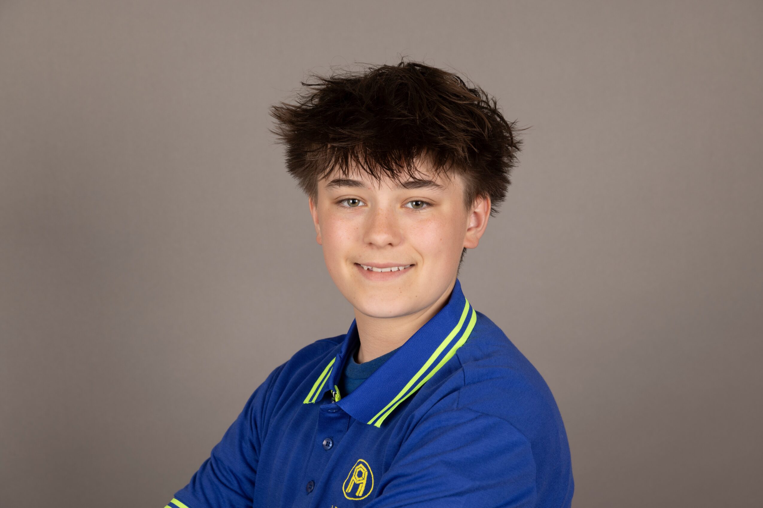 Young boy with messy hair smiling, wearing a blue jacket with yellow and green stripes, against a plain background.