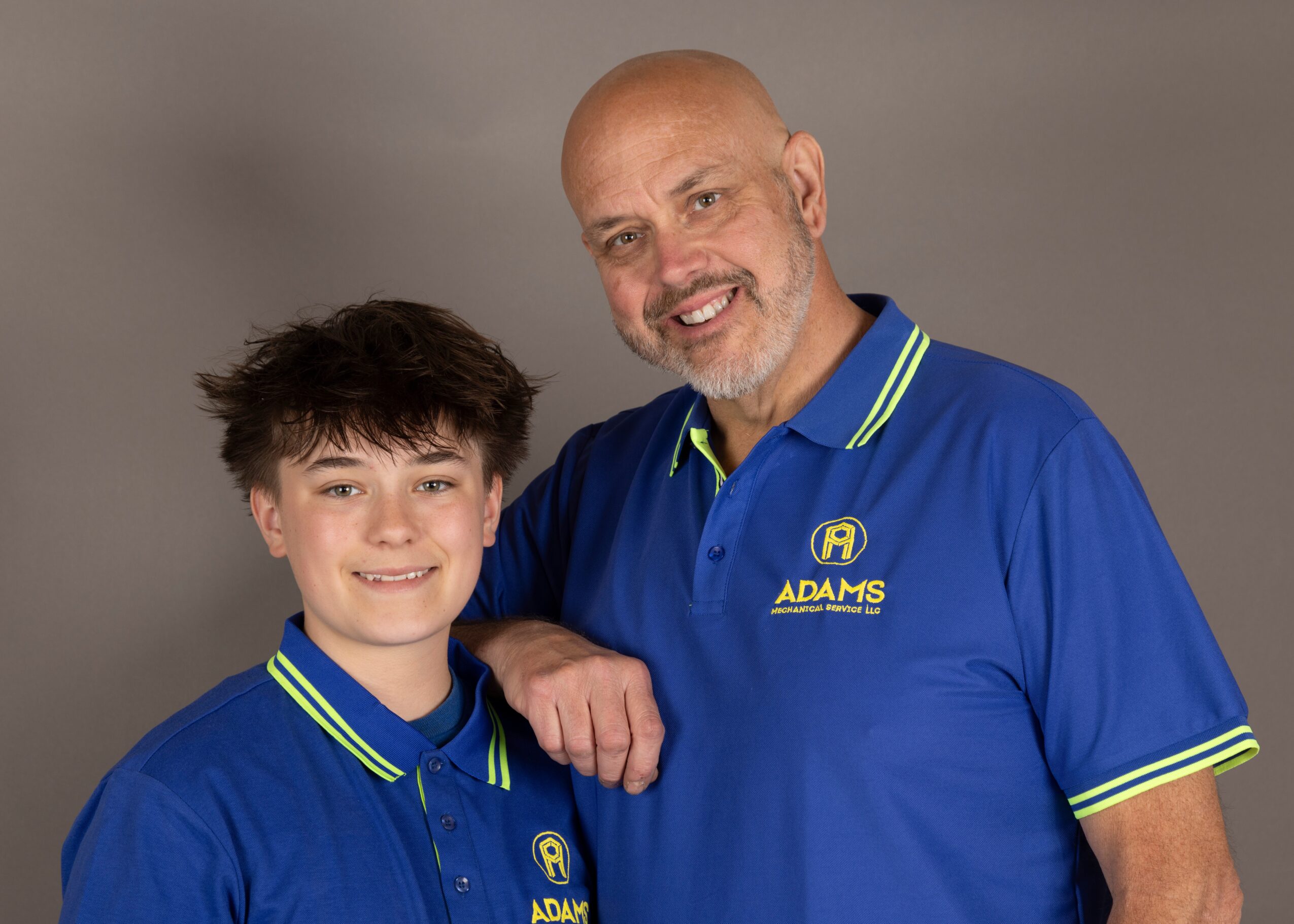 Two people, a young boy and an older man, wearing matching blue polo shirts with yellow accents, smiling together.