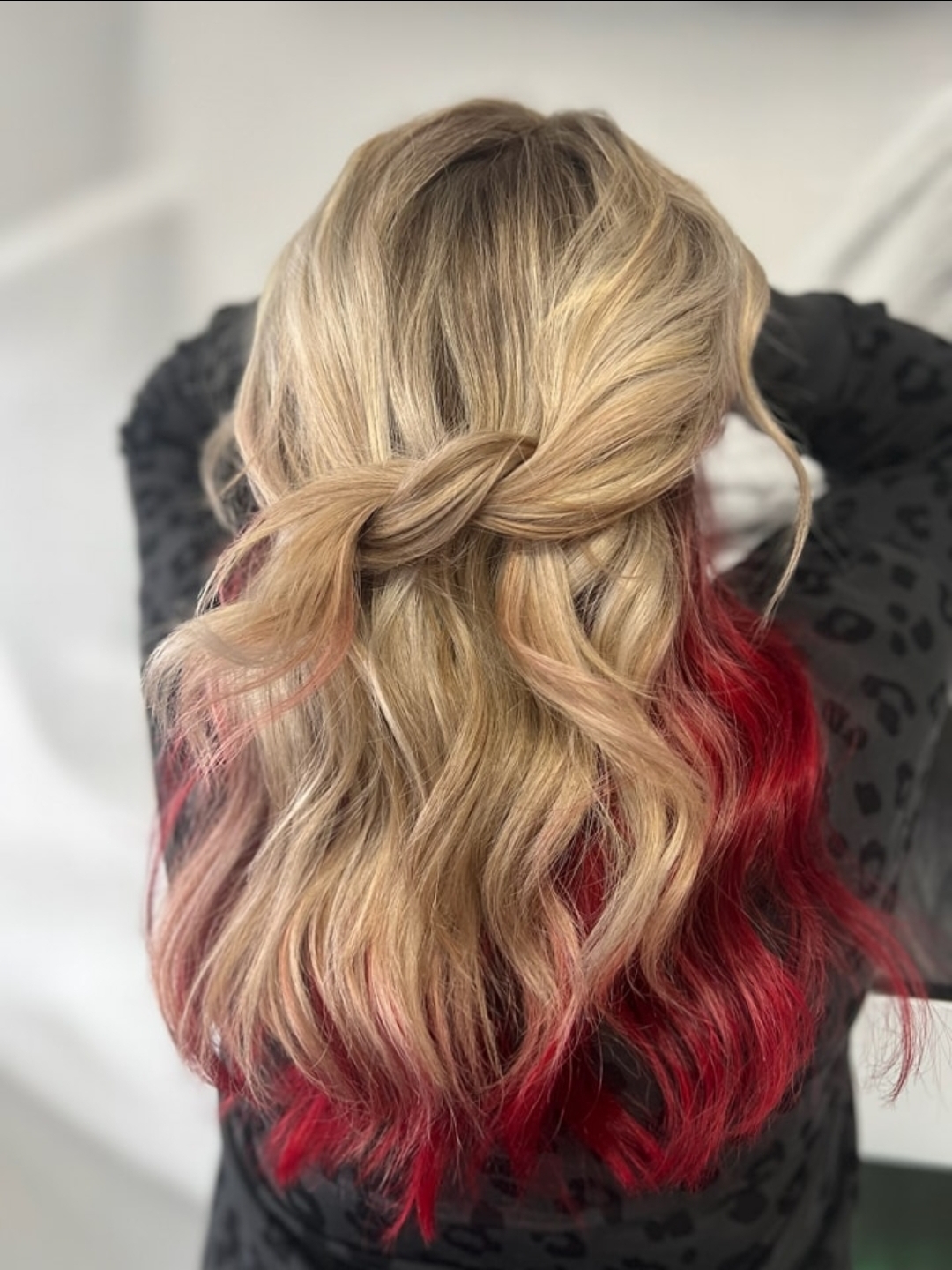 Person with long, wavy hair styled with a braid, hair color transitions from blonde to red at the ends.