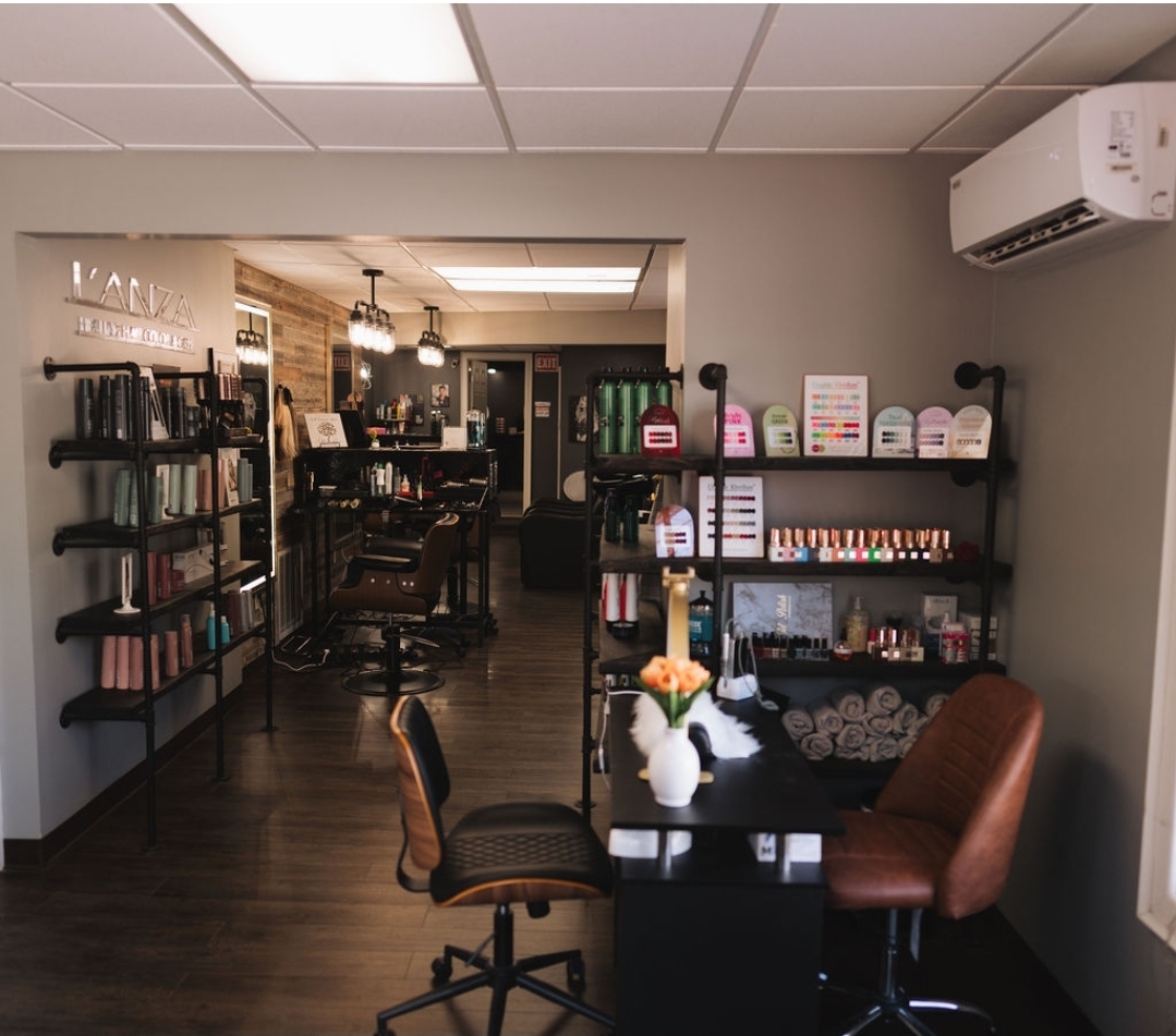 Interior of a salon with chairs, shelves, and a reception desk, illuminated by ceiling lights and natural light from a window.