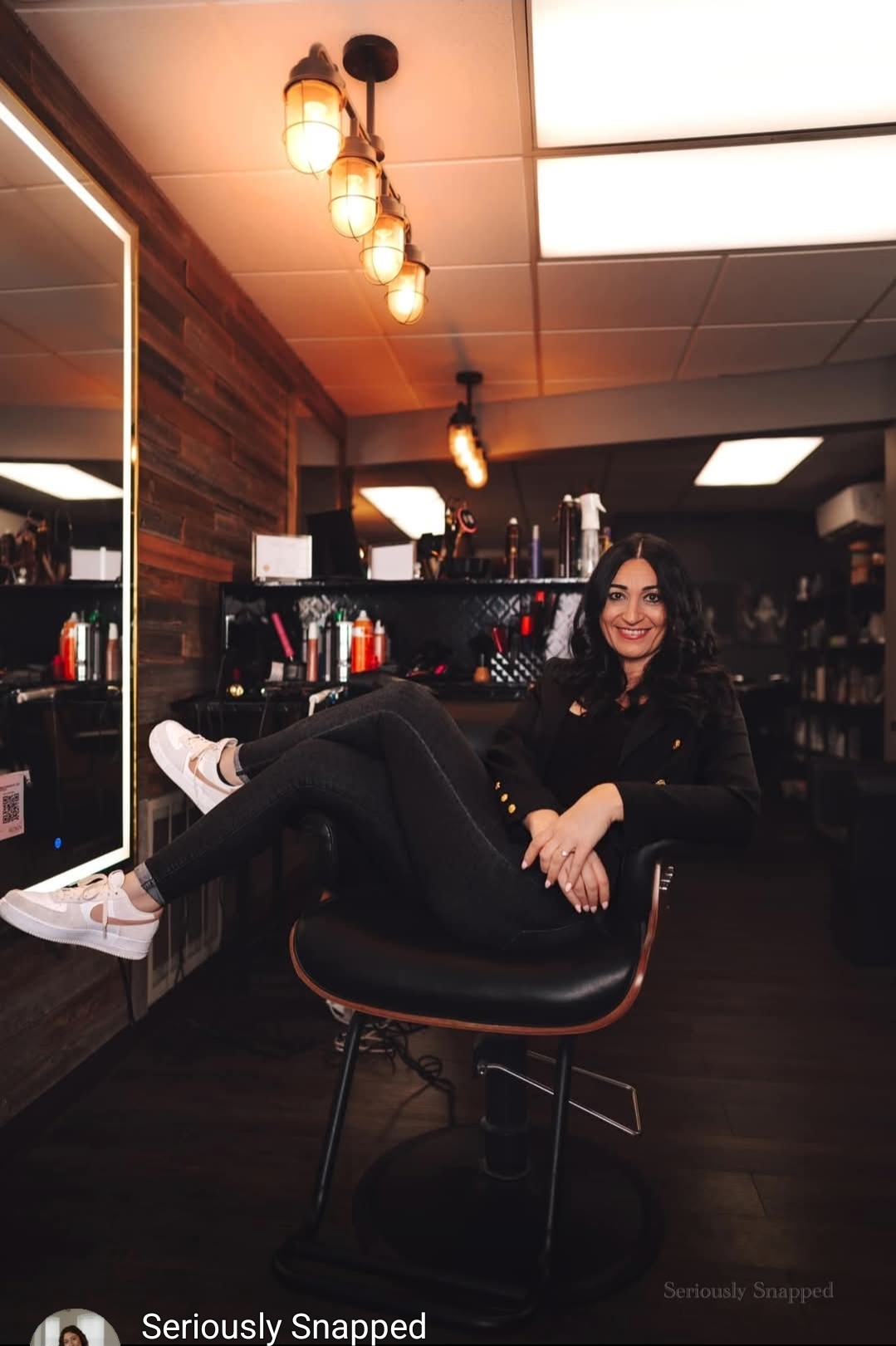 Woman sitting on a chair in a store, smiling, with shelves and lighting in the background.