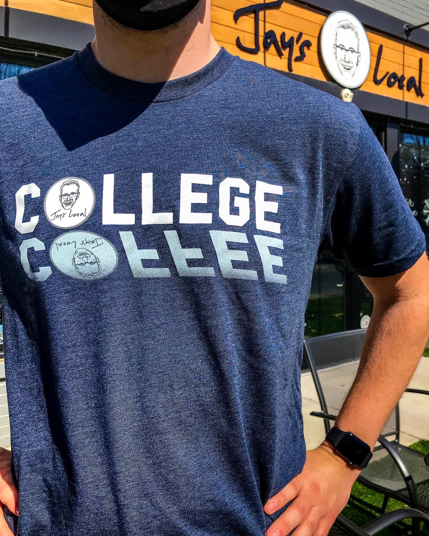 Person wearing a blue T-shirt with white text and graphics, standing outside a restaurant with an orange sign.