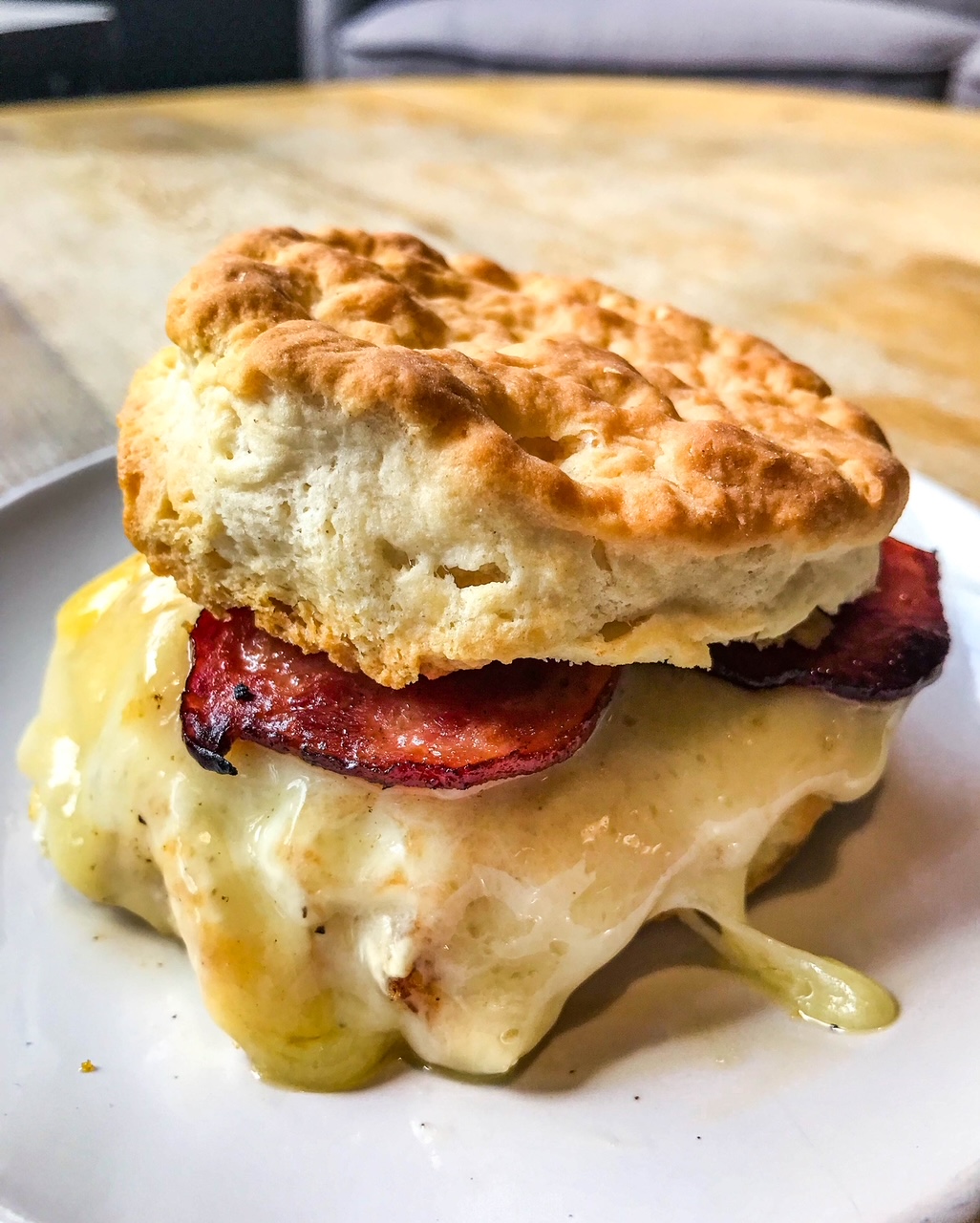A biscuit sandwich with melted cheese, bacon, and biscuit on top, served on a white plate.
