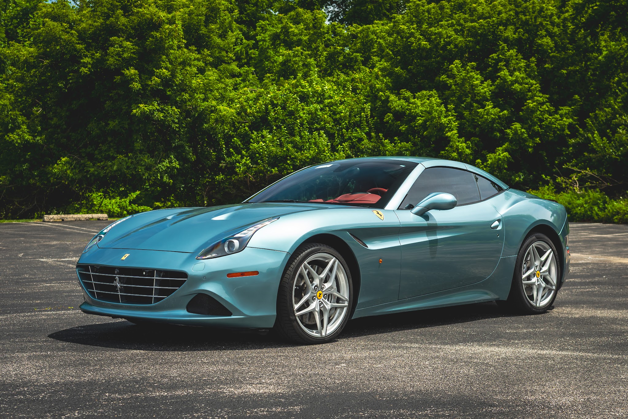 A blue sports car parked on asphalt with green trees in the background.