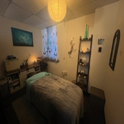 A cozy bedroom with a bed, a window with curtains, a shelf with decorative items, and a wall mirror.