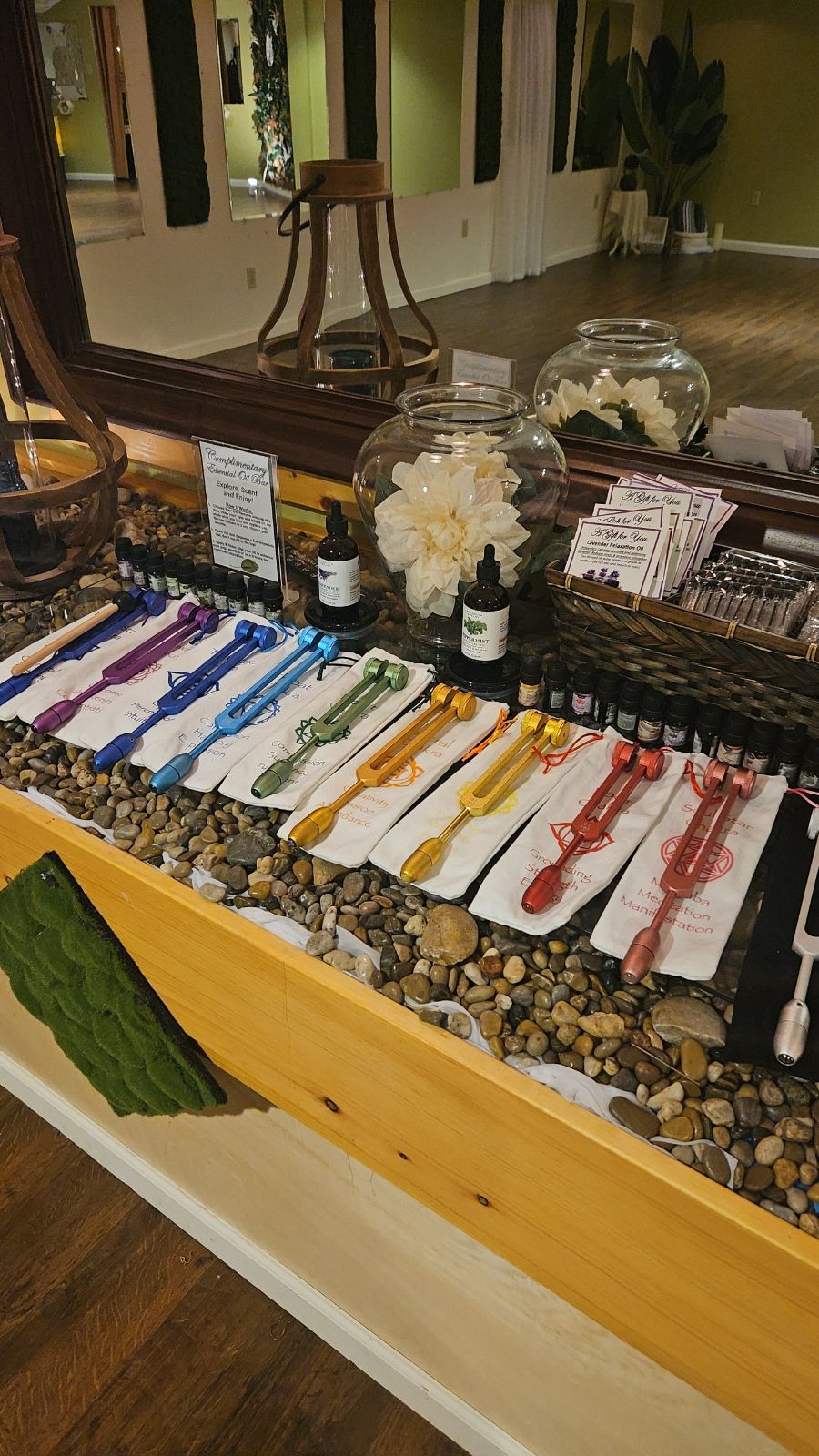 Display of colorful necklaces on a table with a pebble surface, mirror, and decorative items in the background.