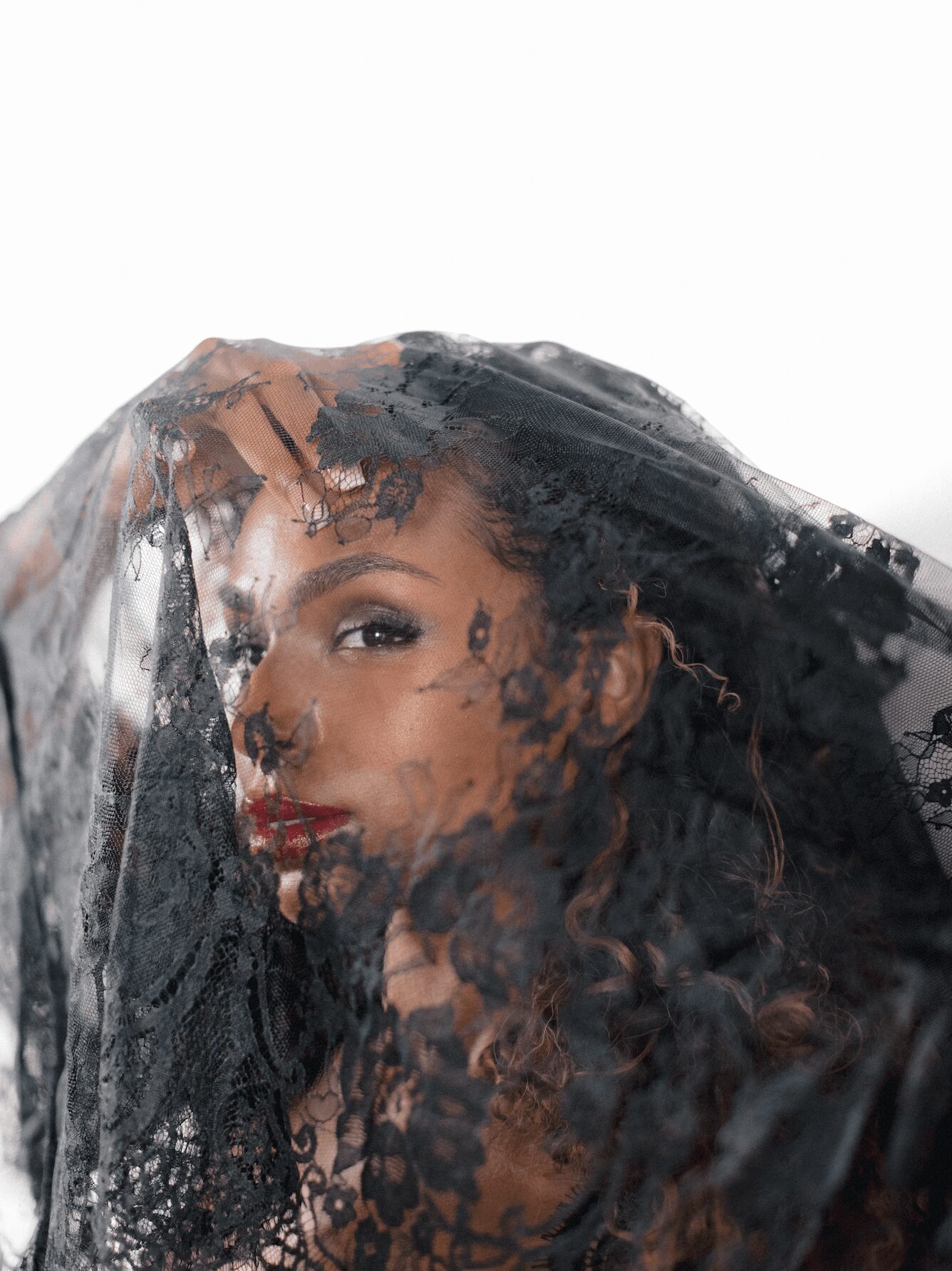 Woman with curly hair and makeup behind a transparent plastic sheet, partially obscuring her face.