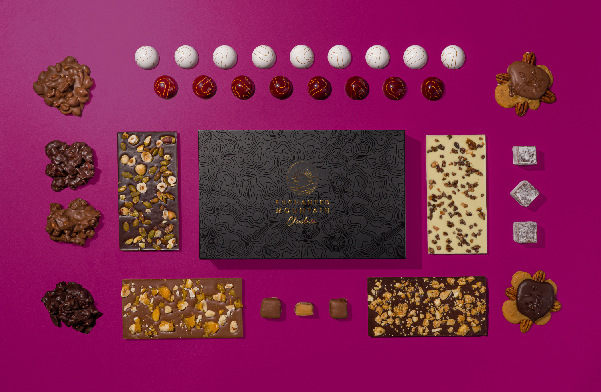 Assorted chocolates and confections arranged on a pink background, including truffles, pralines, and chocolate bars.