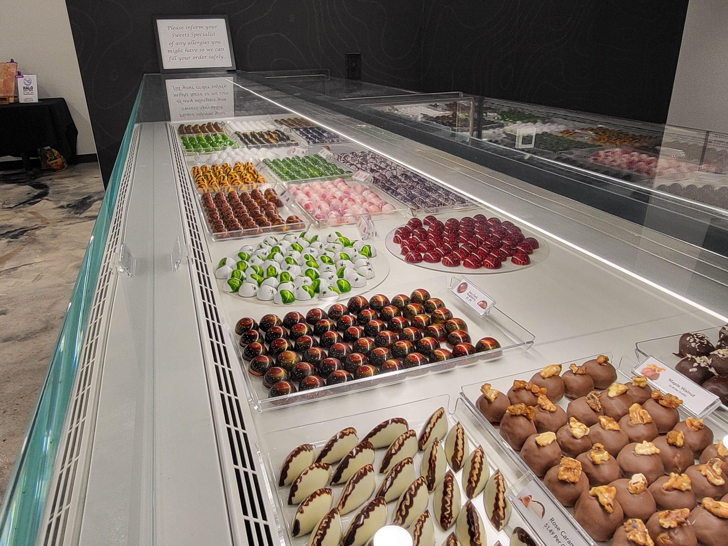 Display case with various colorful desserts and chocolates arranged in rows inside a store.