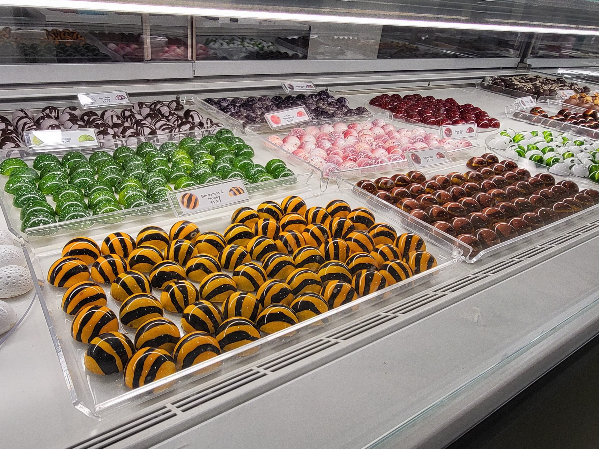 Display of colorful chocolates and candies in a store, including green, pink, brown, and yellow with black striped candies.