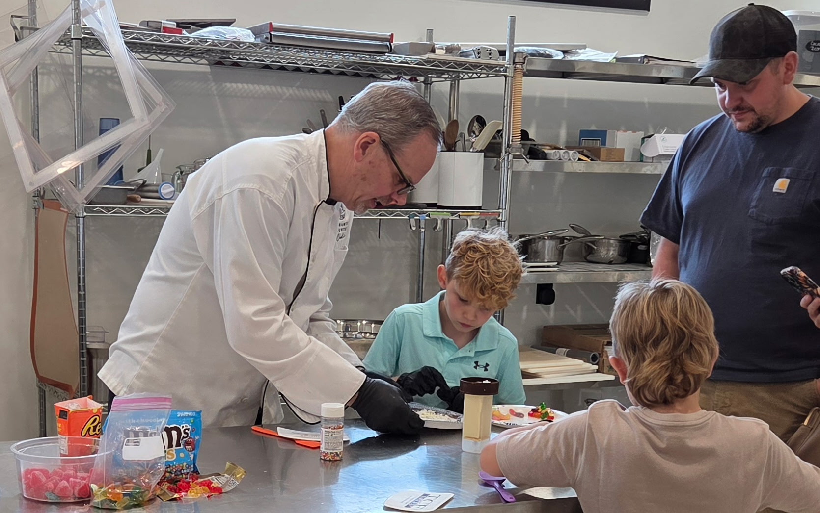 A scientist in a white lab coat and gloves demonstrates an experiment to two children in a laboratory setting.