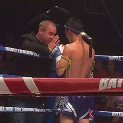 Boxer and coach in a ring, coach whispering to boxer with back turned, boxing ring ropes visible.