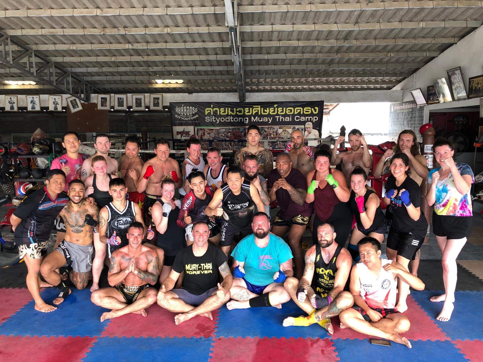 Group of people in a martial arts training facility, some in fighting stances, with a banner in the background.