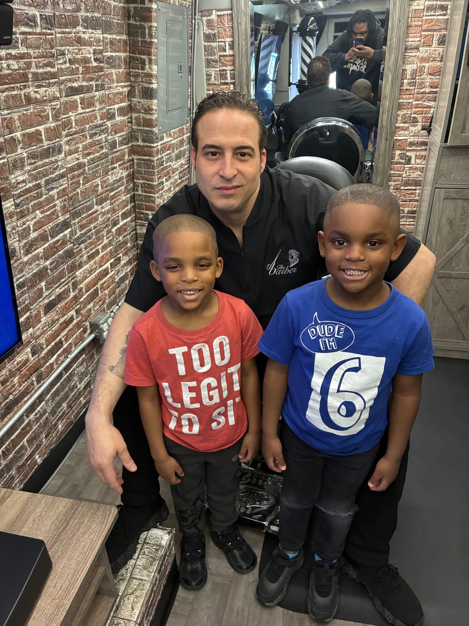 Three children and an adult standing inside a brick-walled room, smiling at the camera.