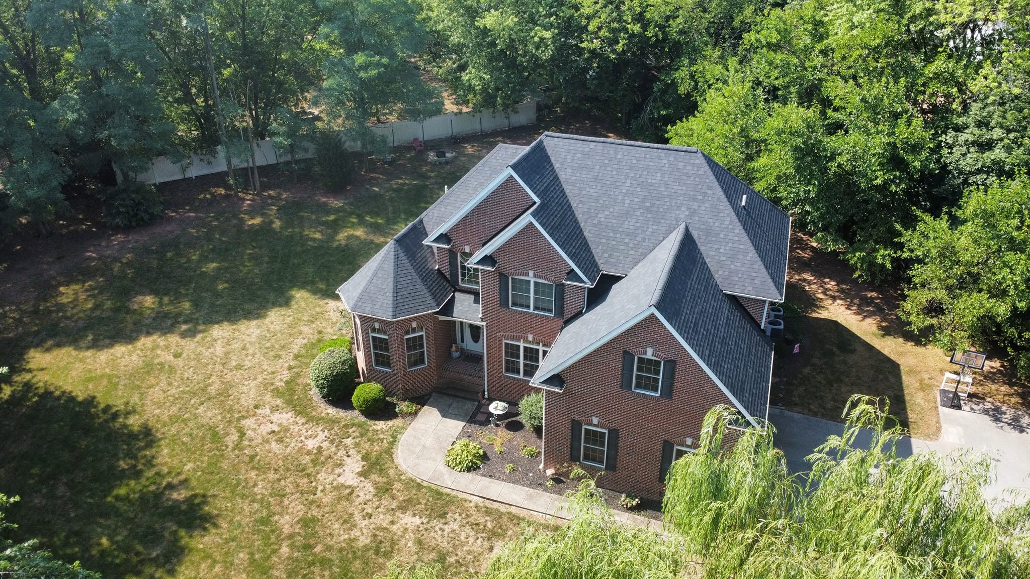 A large brick house with multiple gabled roofs surrounded by trees and a lawn, viewed from above.