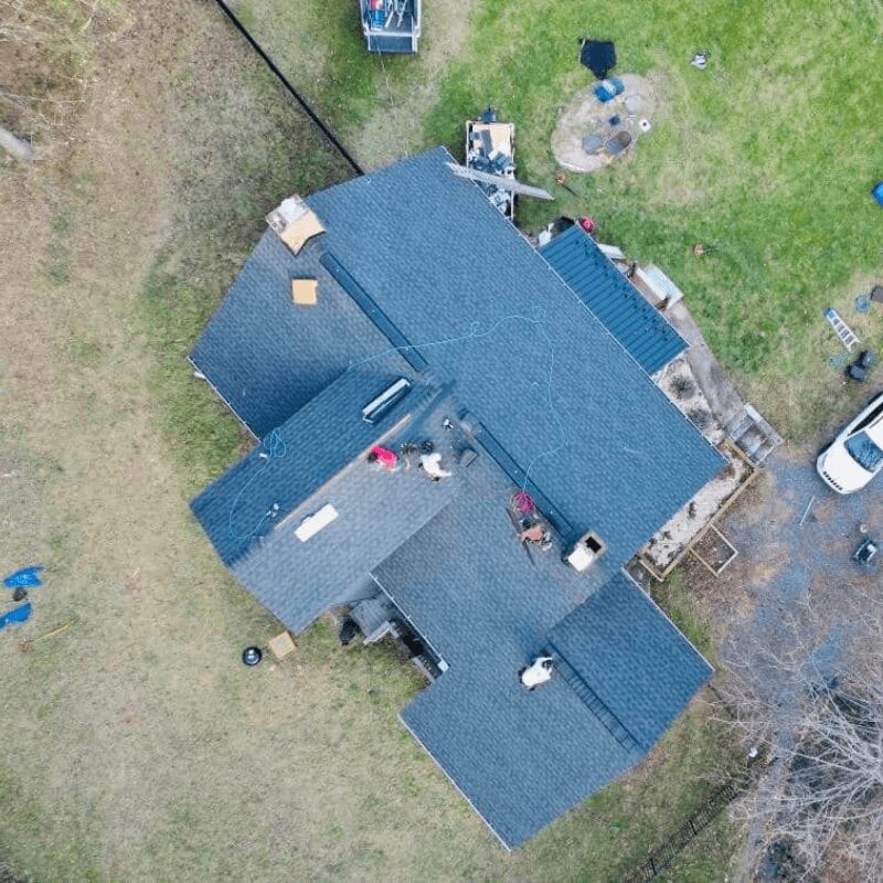 A house with a dark roof, surrounded by a yard with grass and a driveway, viewed from above.