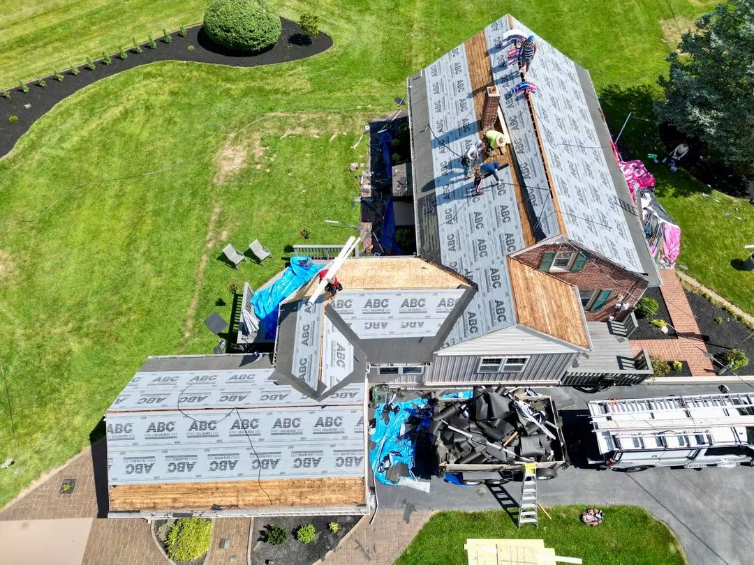 Construction site with a partially built house, construction materials, and equipment on a grassy area.