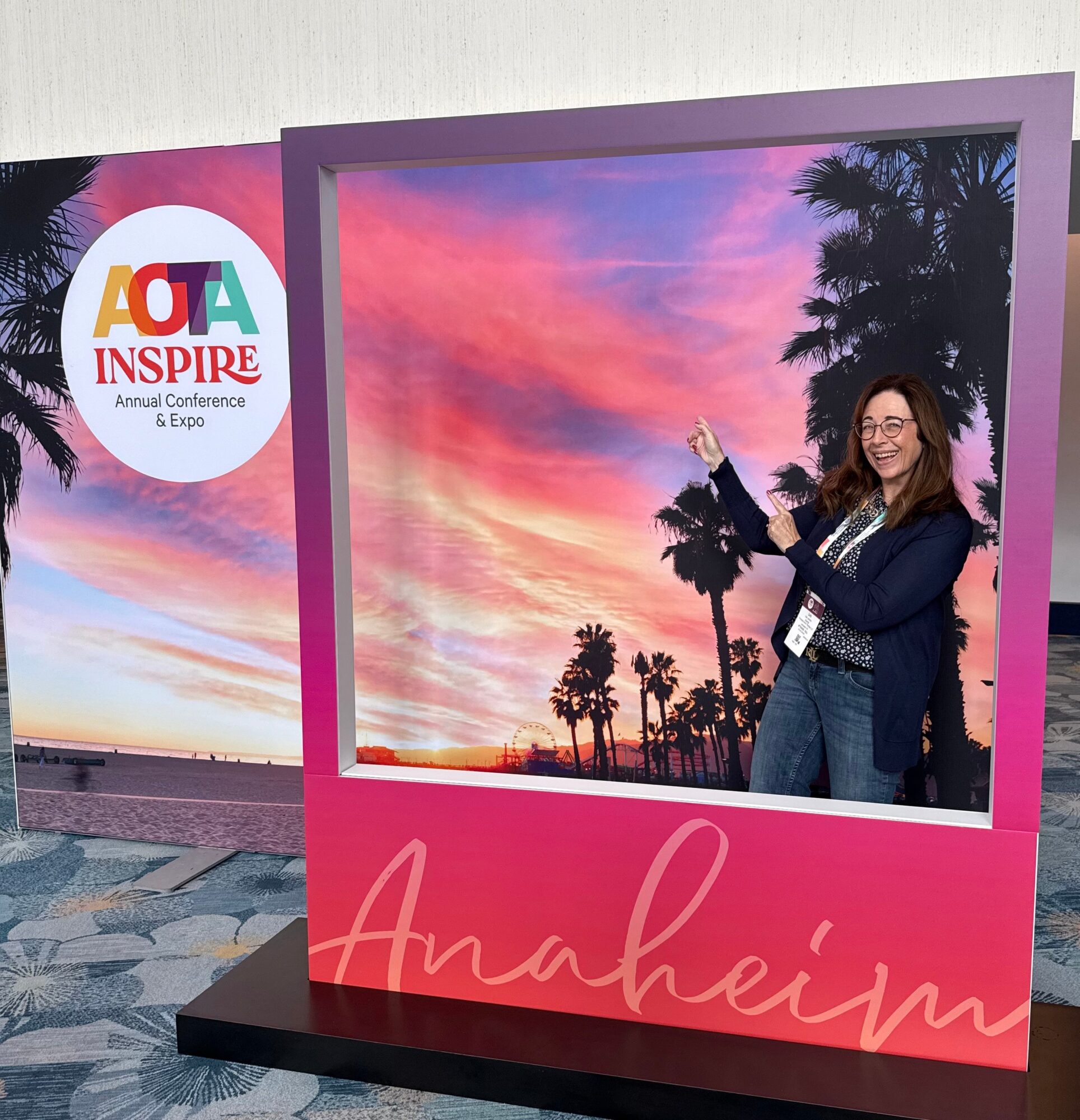 Woman standing next to a sunset-themed photo display with palm trees, at an event called Inspire in Anaheim.