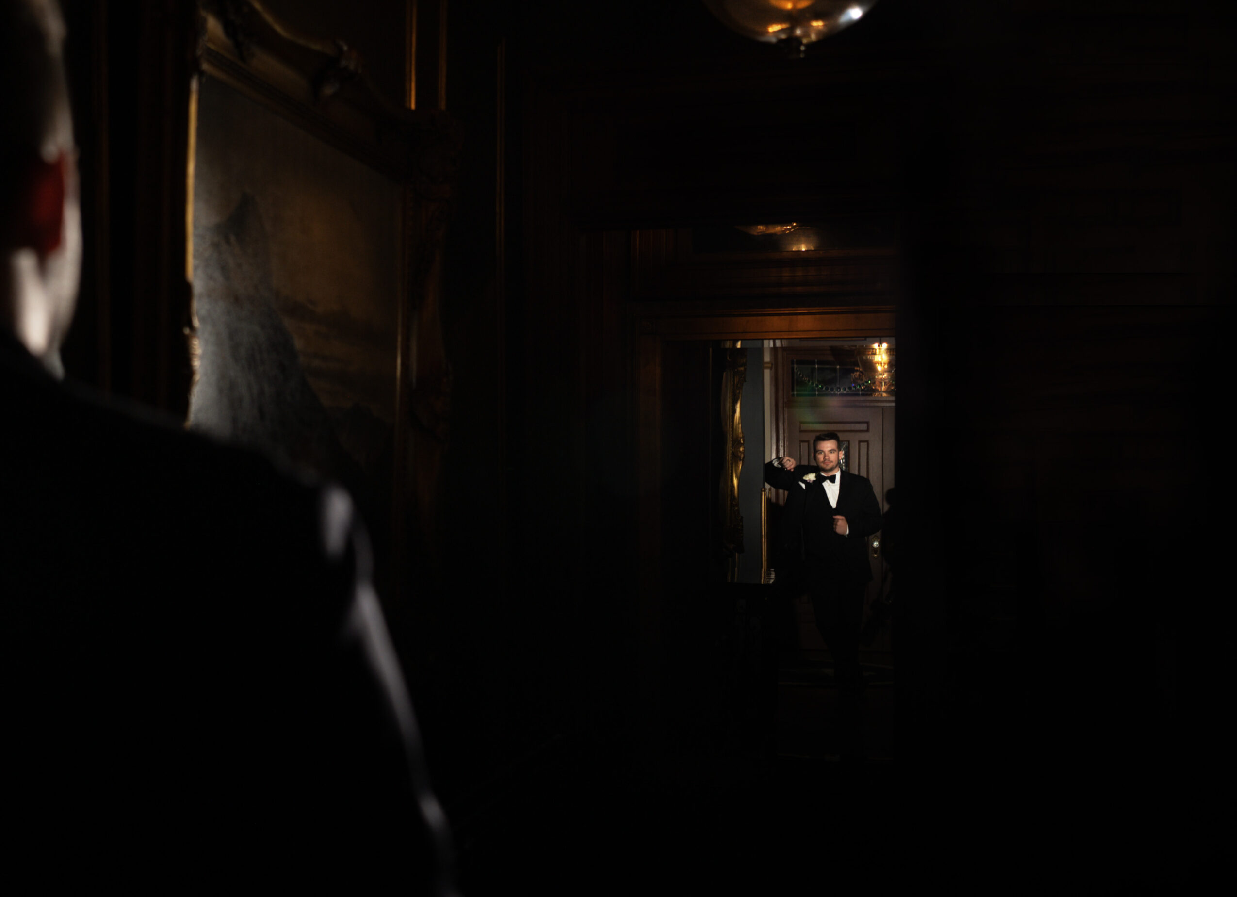 Person looking at a mirror reflecting another person in a dark room with warm lighting, framed by wooden walls.