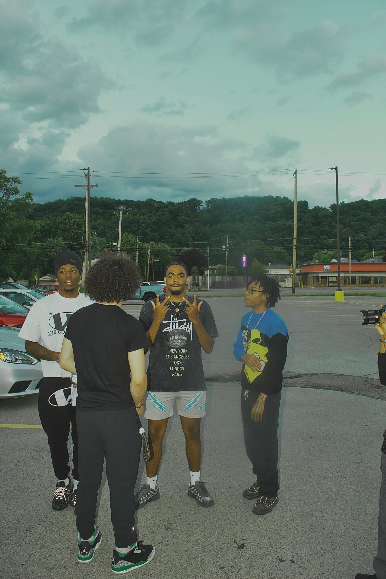 Four people standing and talking in a parking lot with cars and trees in the background.