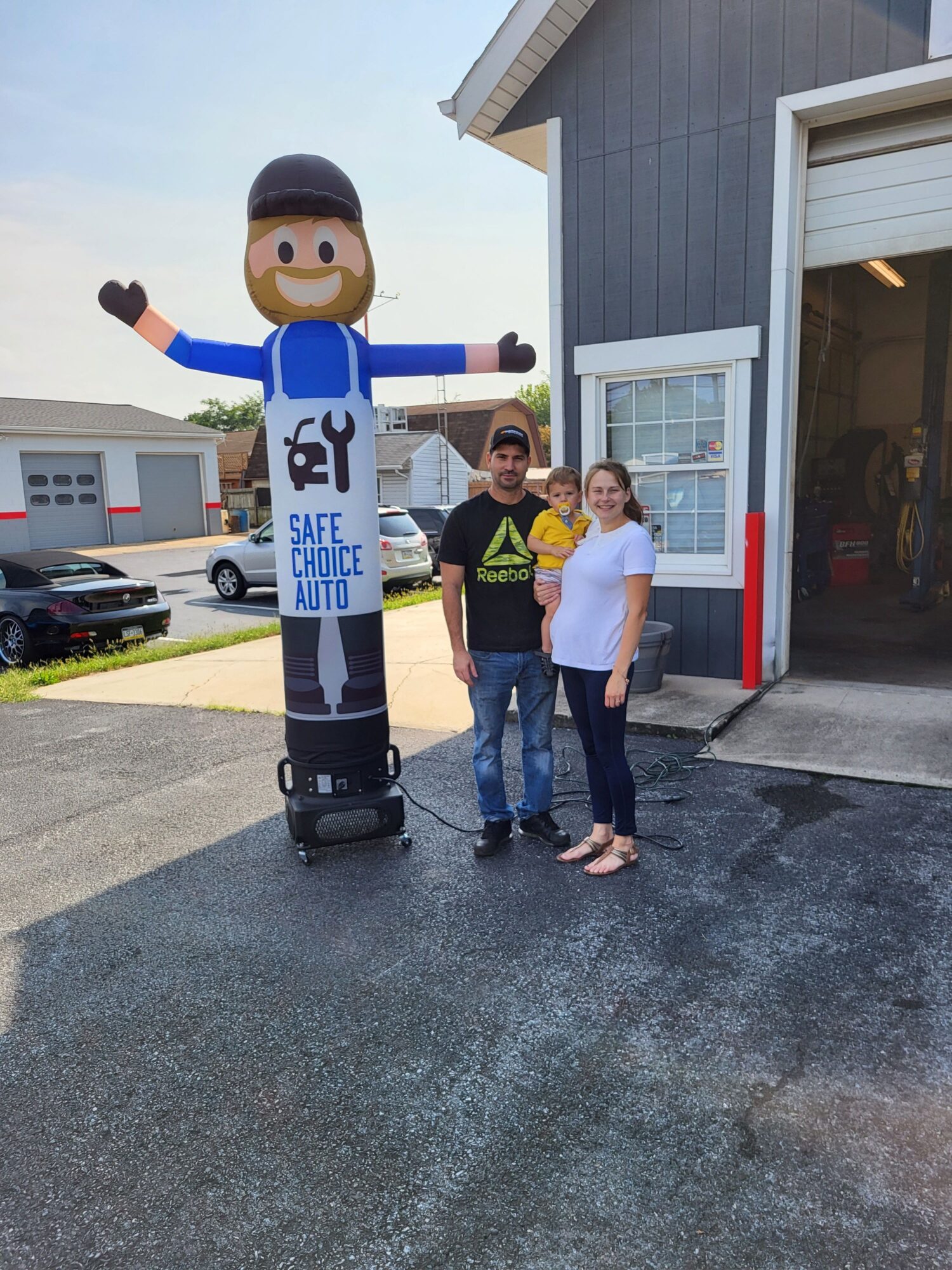 Three people standing outside a building, one in a robot costume, two in casual clothes, on a paved area.