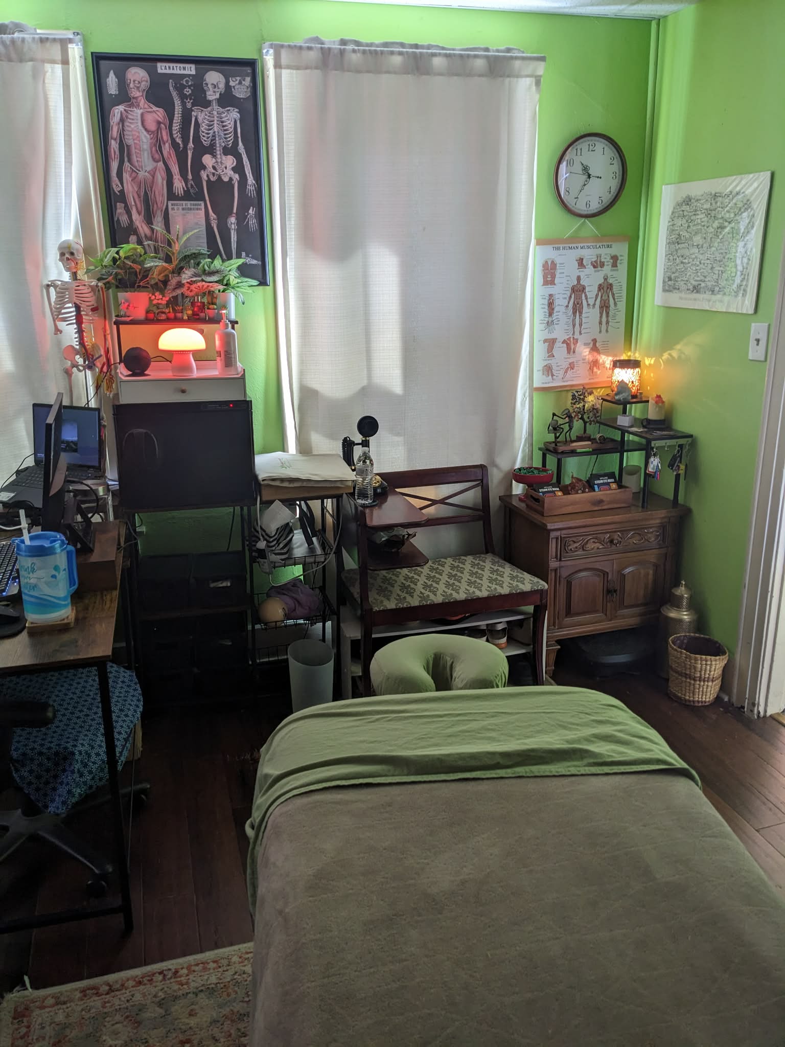 Room with green walls, a bed, a window with curtains, a clock, and various furniture and decorations.