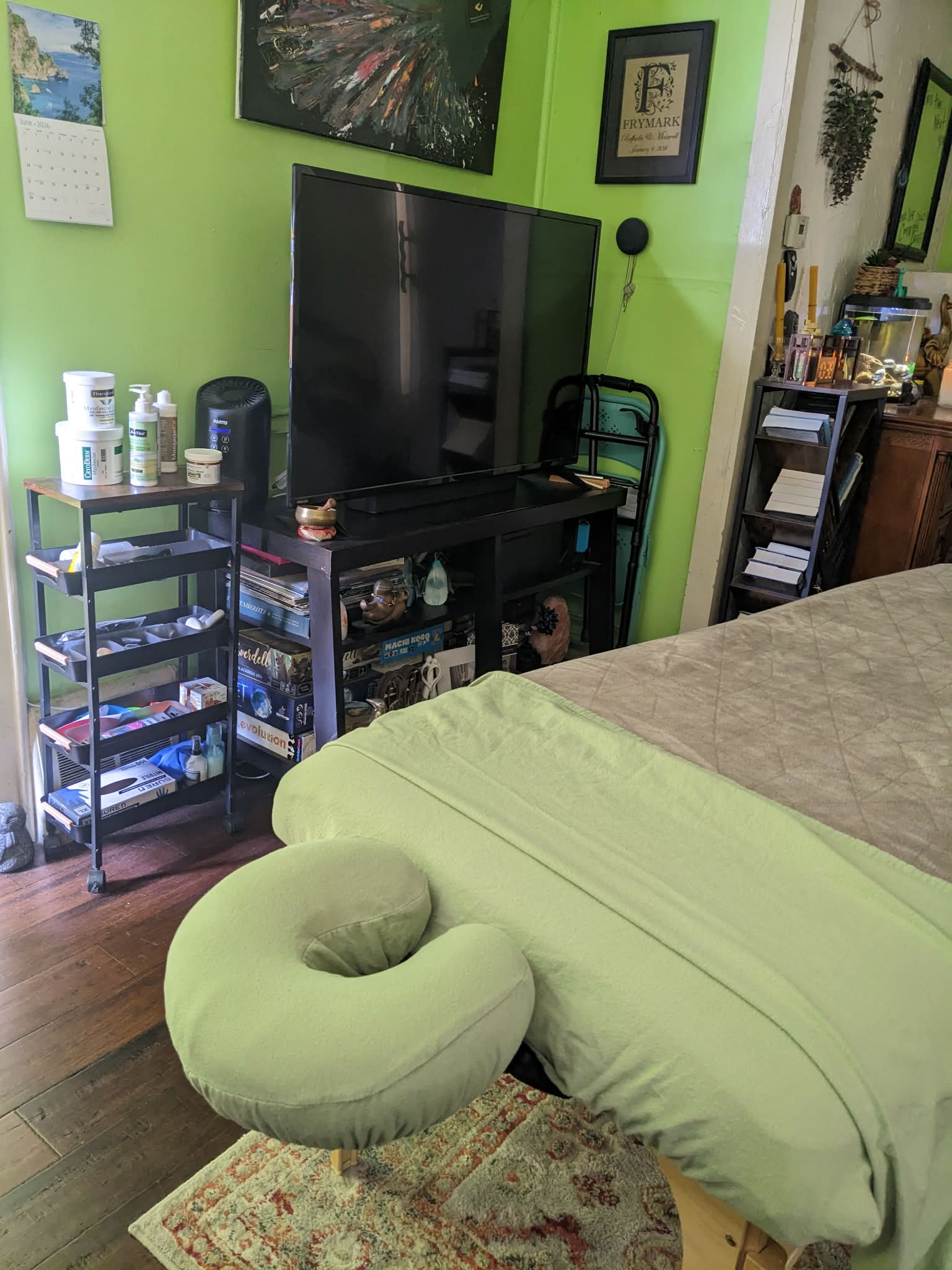 Bedroom with green walls, a bed with a green neck pillow, a TV on a stand, and various furniture and decor.