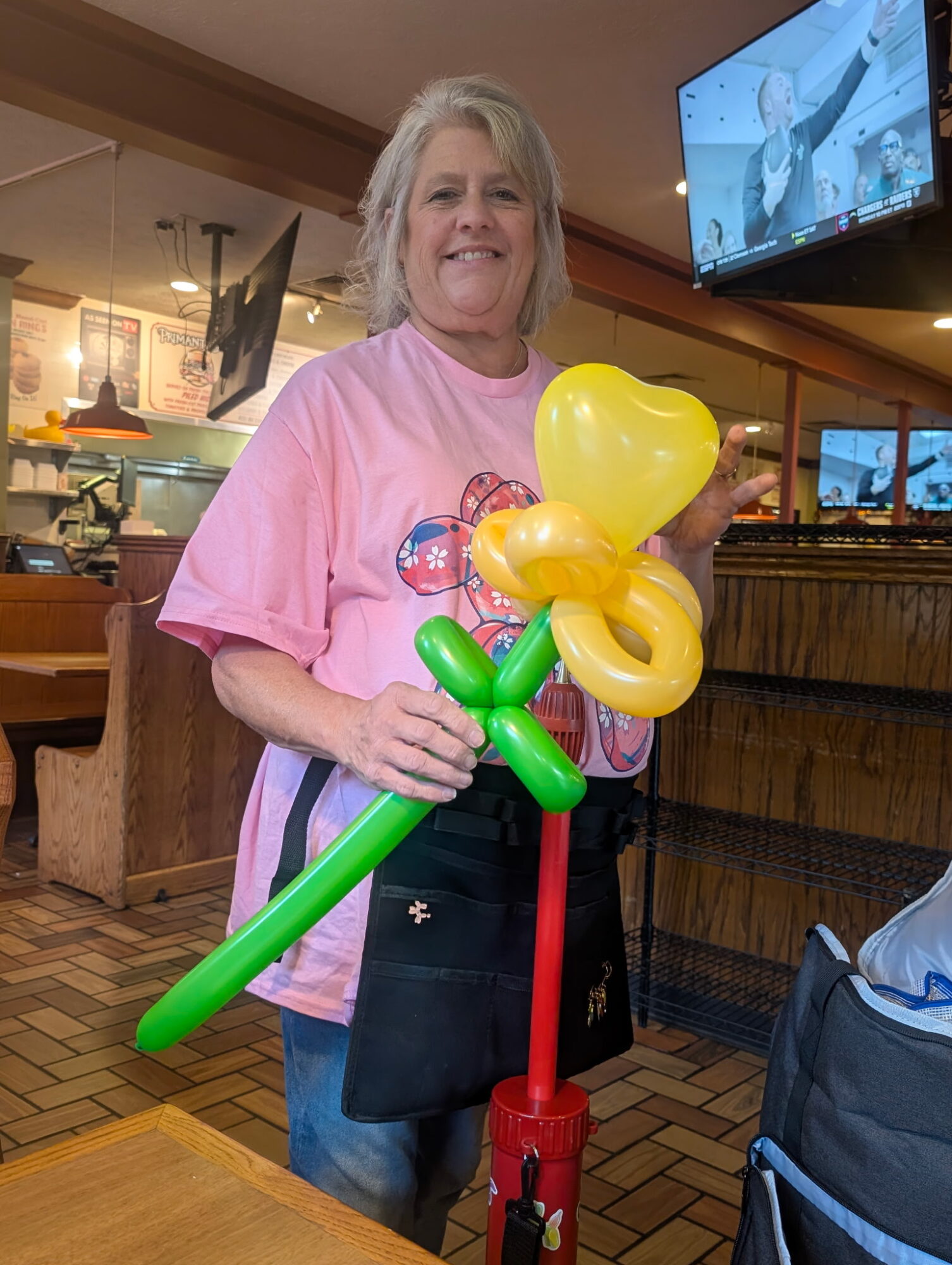 Smiling woman holding yellow balloon flowers in a restaurant, with a TV screen in the background.