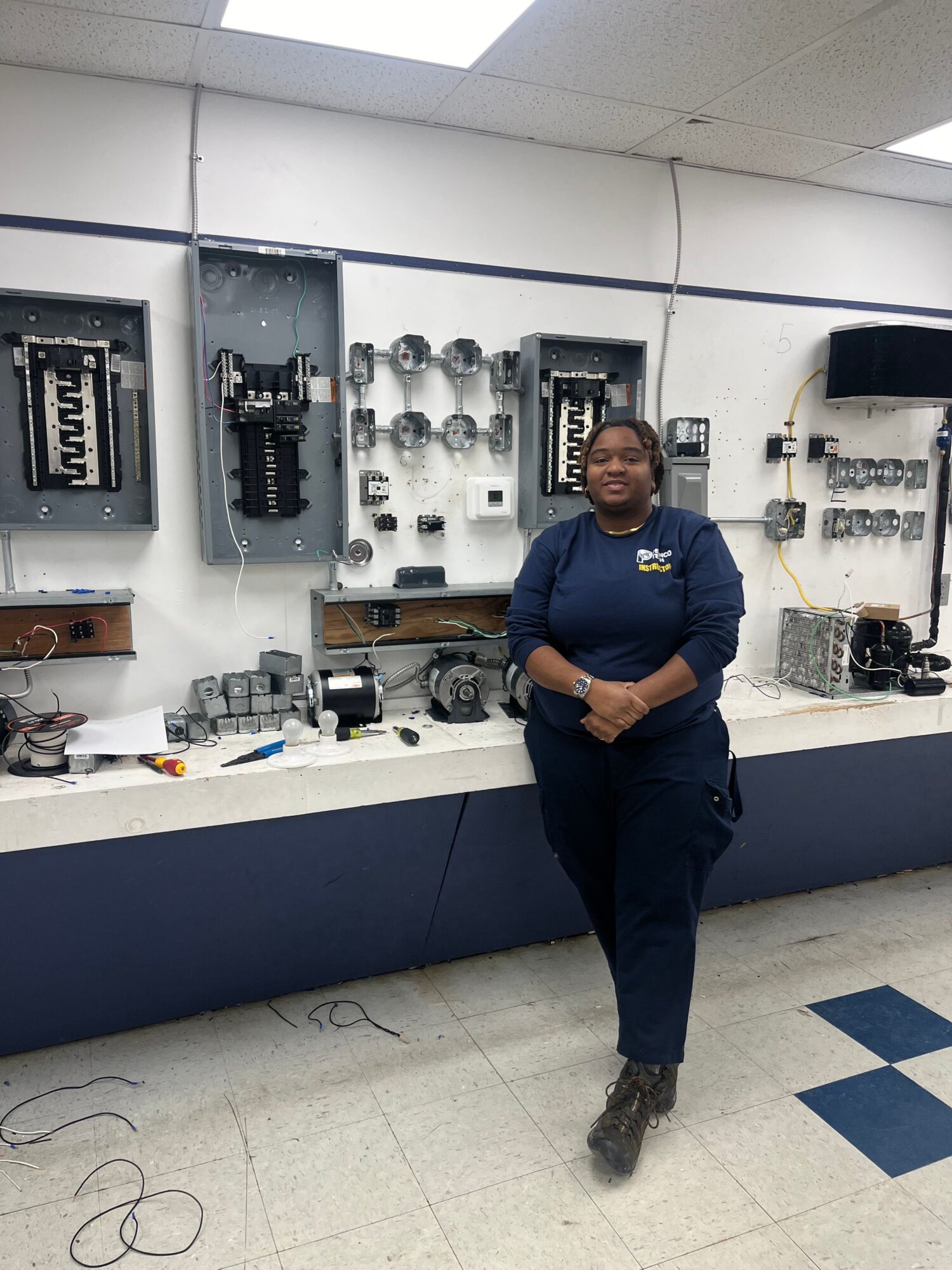 Person in uniform standing in a laboratory with equipment and tools on shelves and workbench.