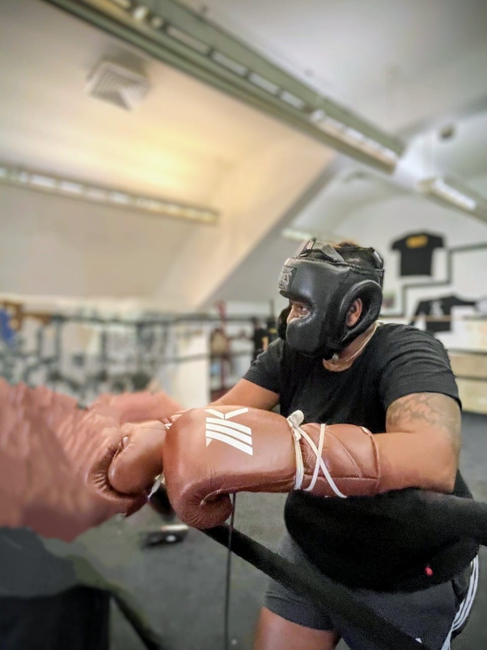 Person wearing a helmet and gloves practicing boxing in a gym, with a punching bag in the background.