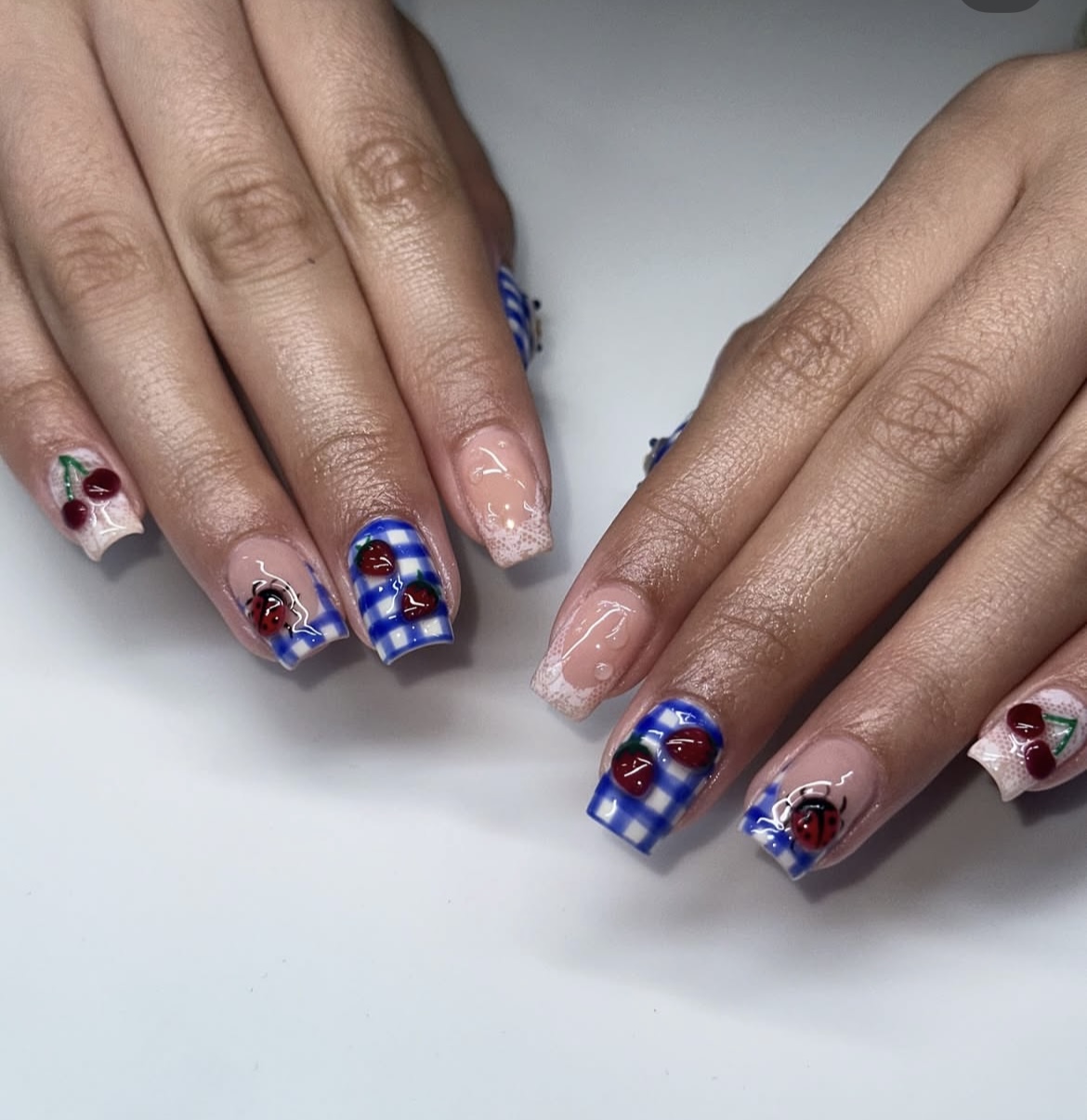 Hands with decorated nails featuring blue, red, and white patterns and small decorative elements, resting on a white surface.